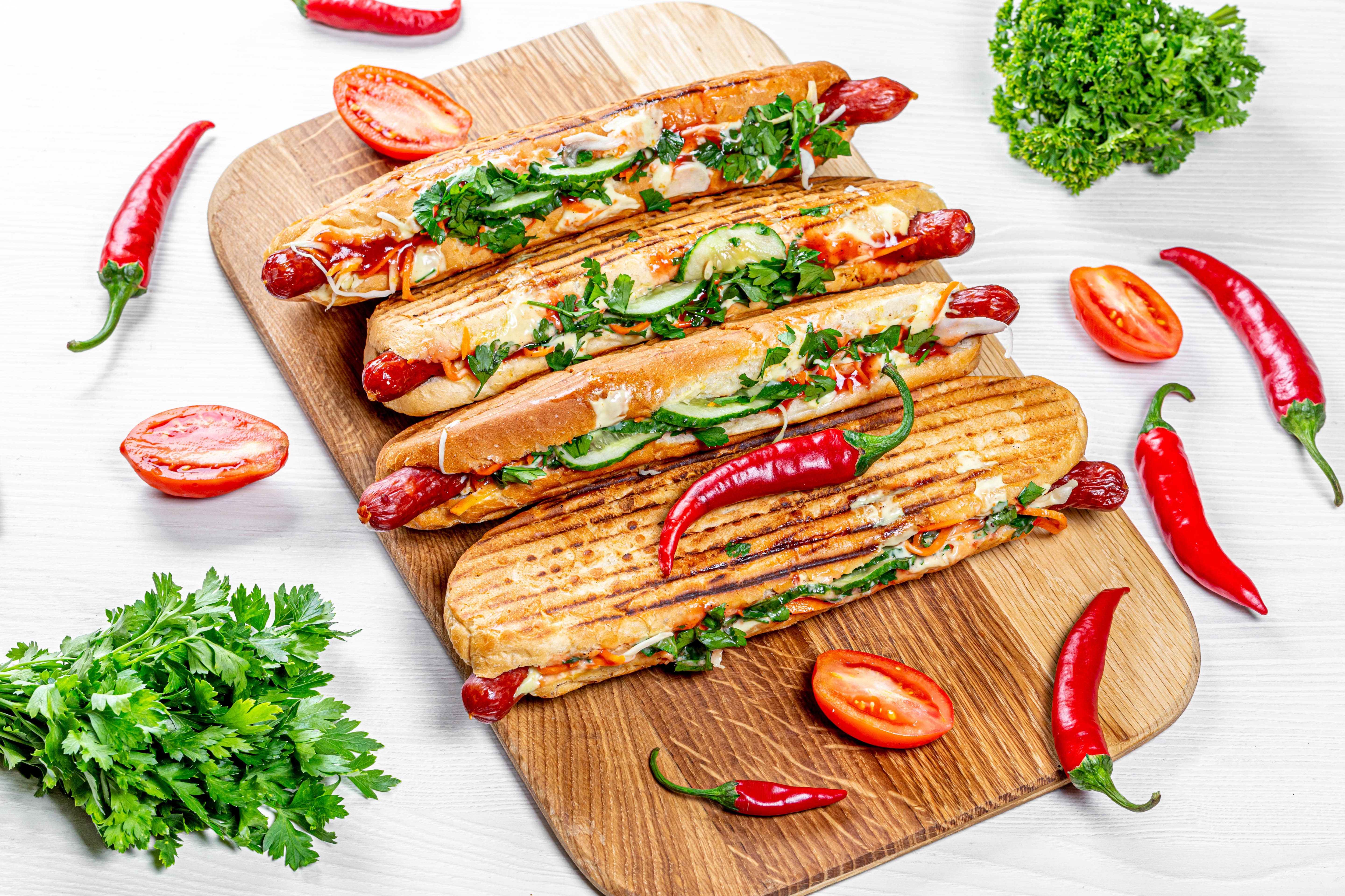 Four hot dogs with chili peppers and tomatoes on a cutting board HD Wallpaper