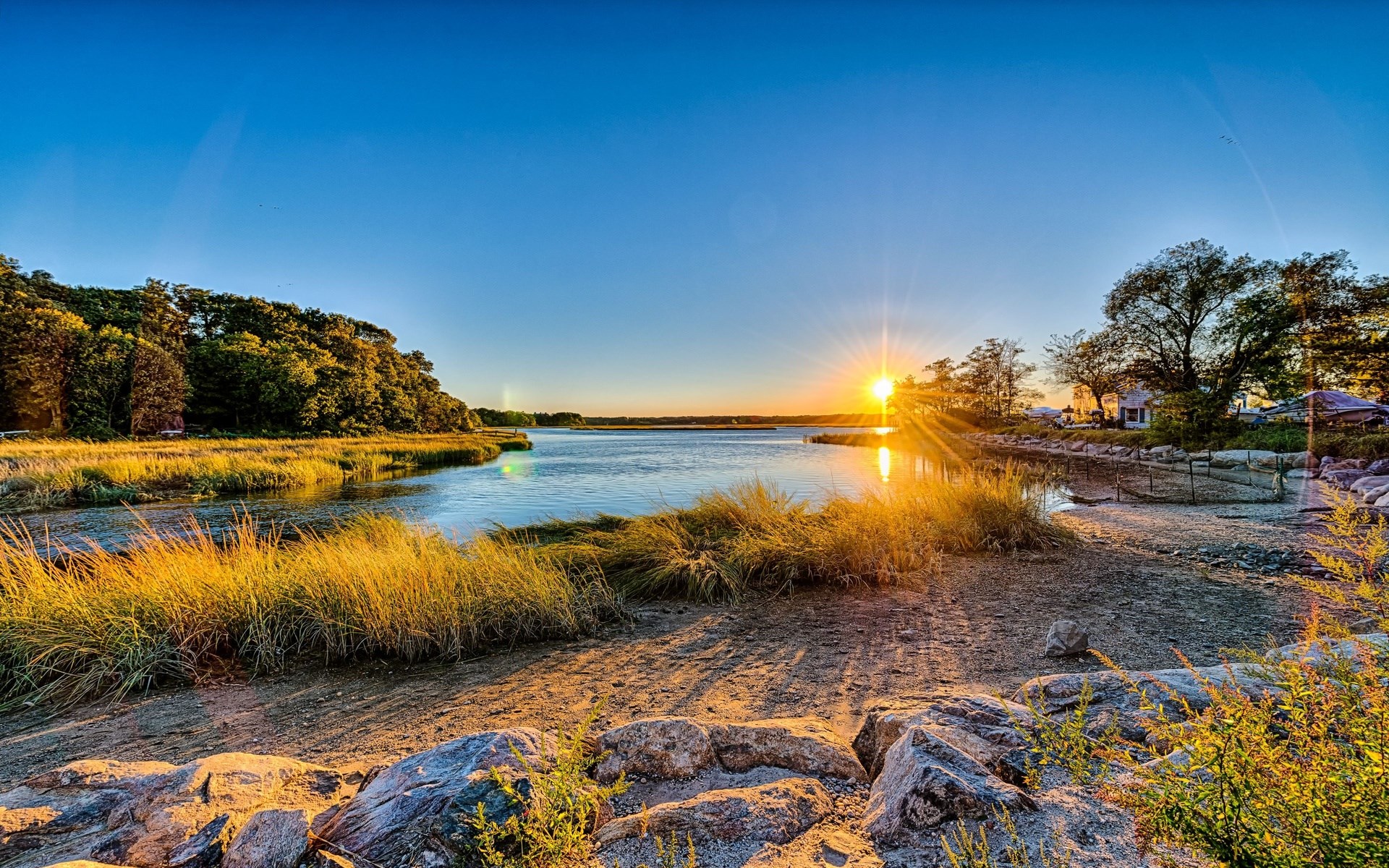 Sunset over a marshy coastline with trees and houses HD Wallpaper