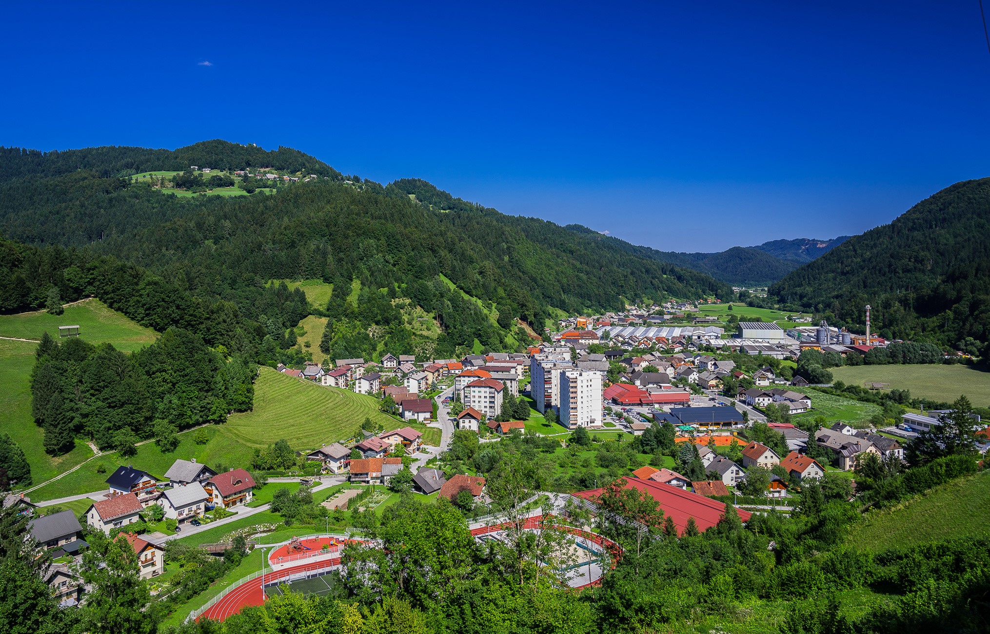 Town nestled in a green valley with forested hills HD Wallpaper