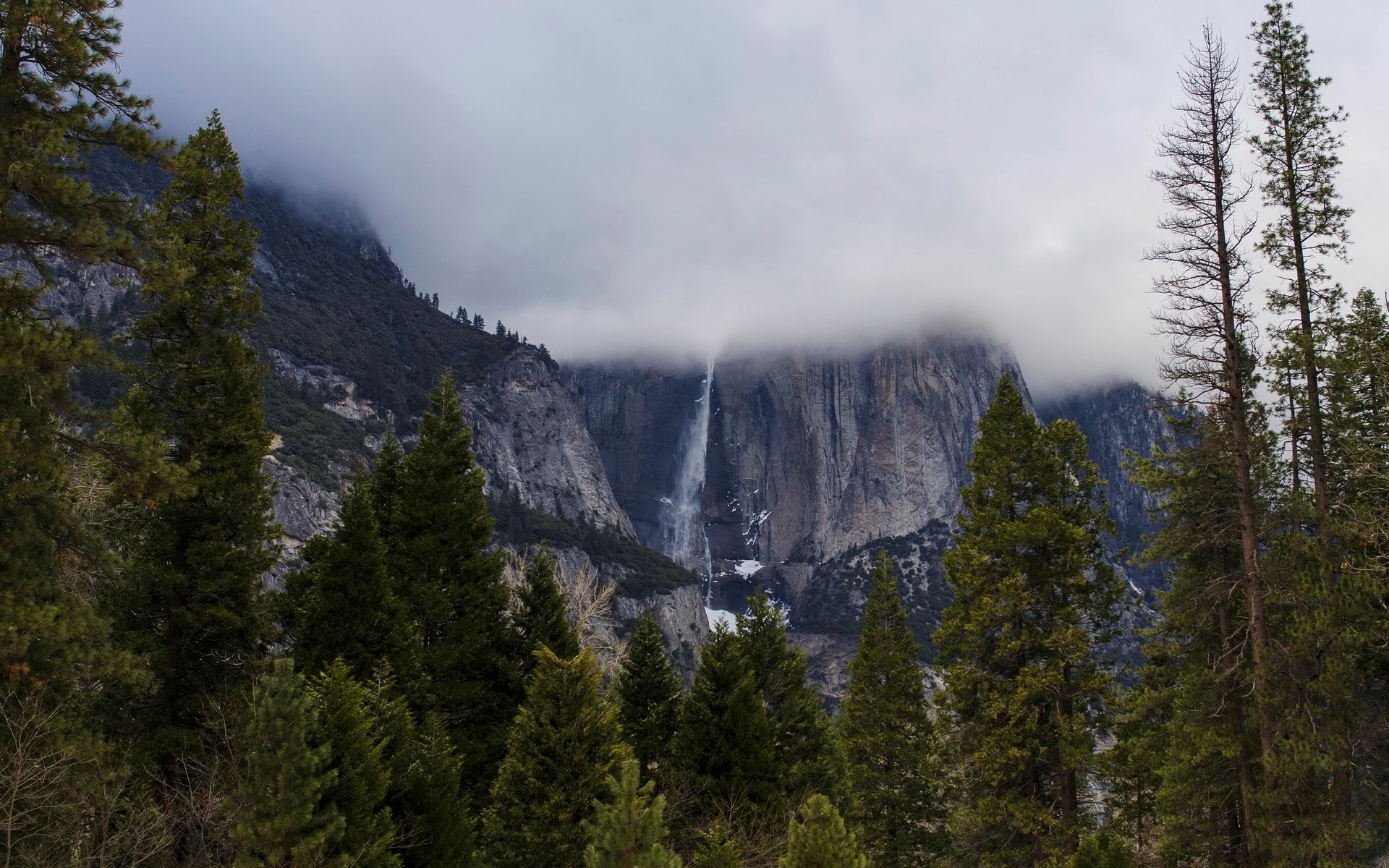 Waterfall cascading down a rocky mountain shrouded in clouds HD Wallpaper
