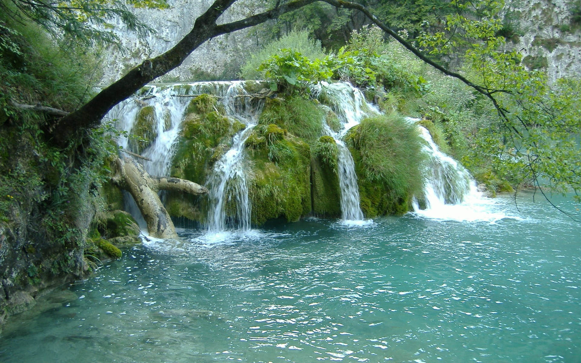 Turquoise water flows over moss-covered rocks in a waterfall HD Wallpaper