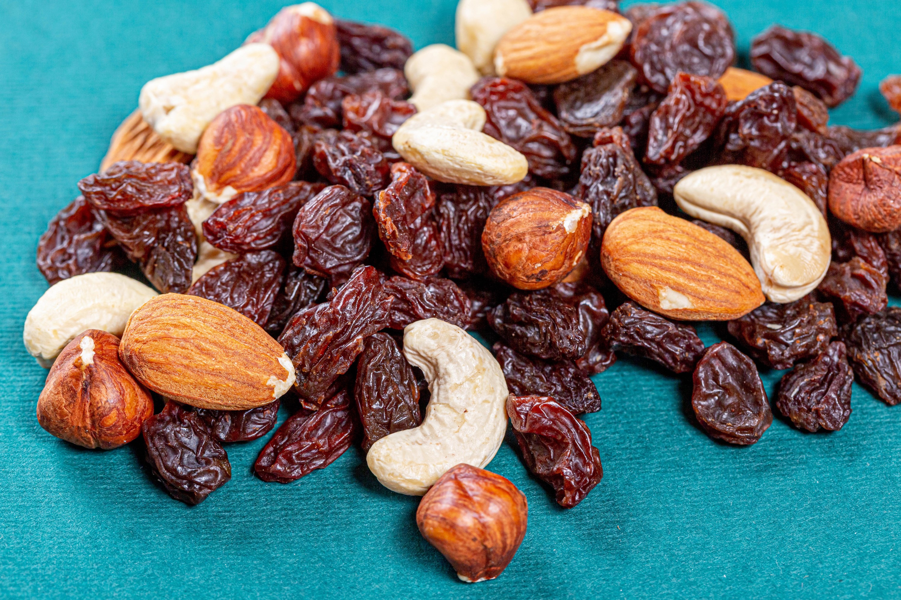 Mixed nuts and raisins on a teal background HD Wallpaper