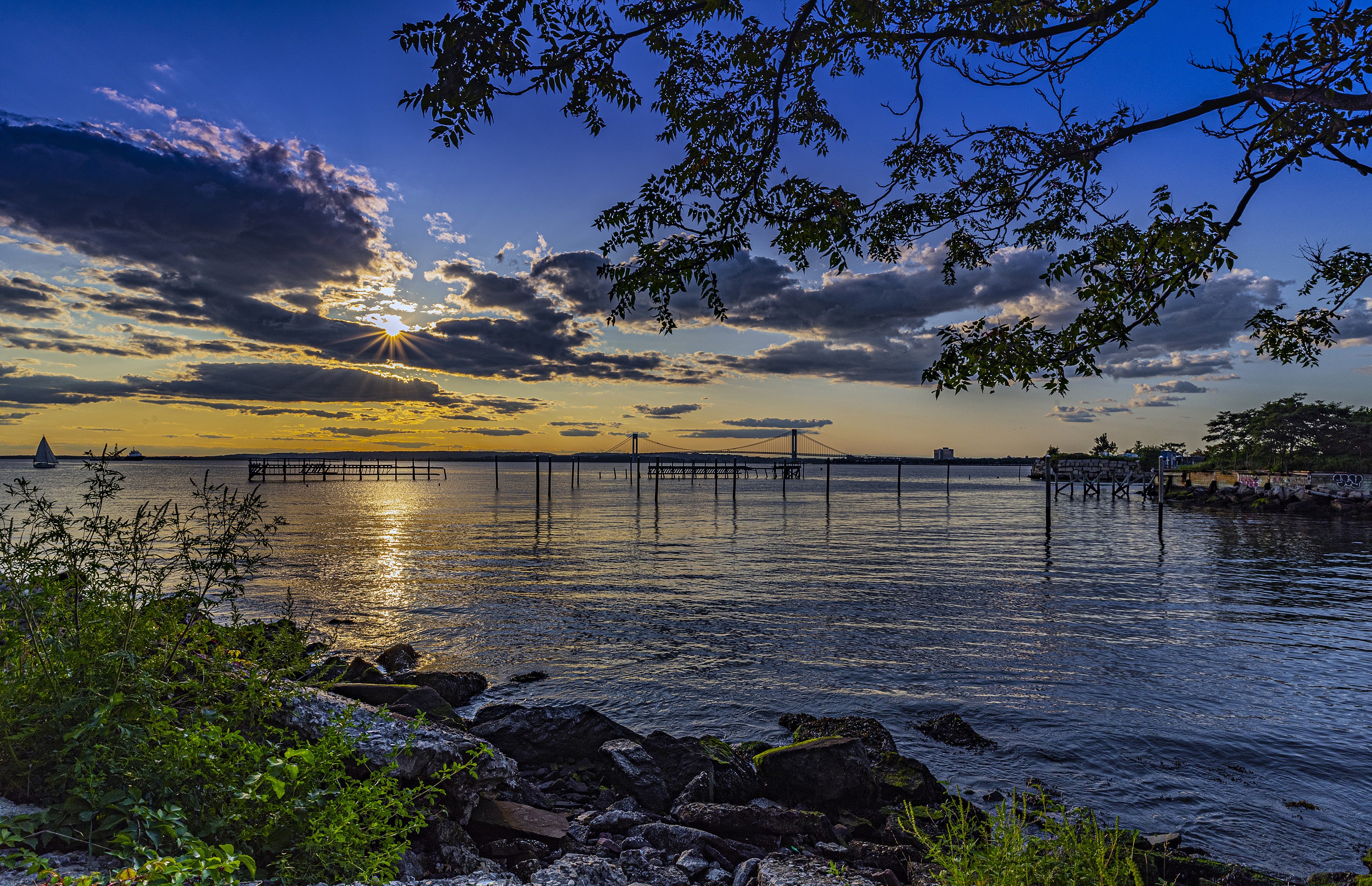 Sunset over water with bridge and sailboat HD Wallpaper