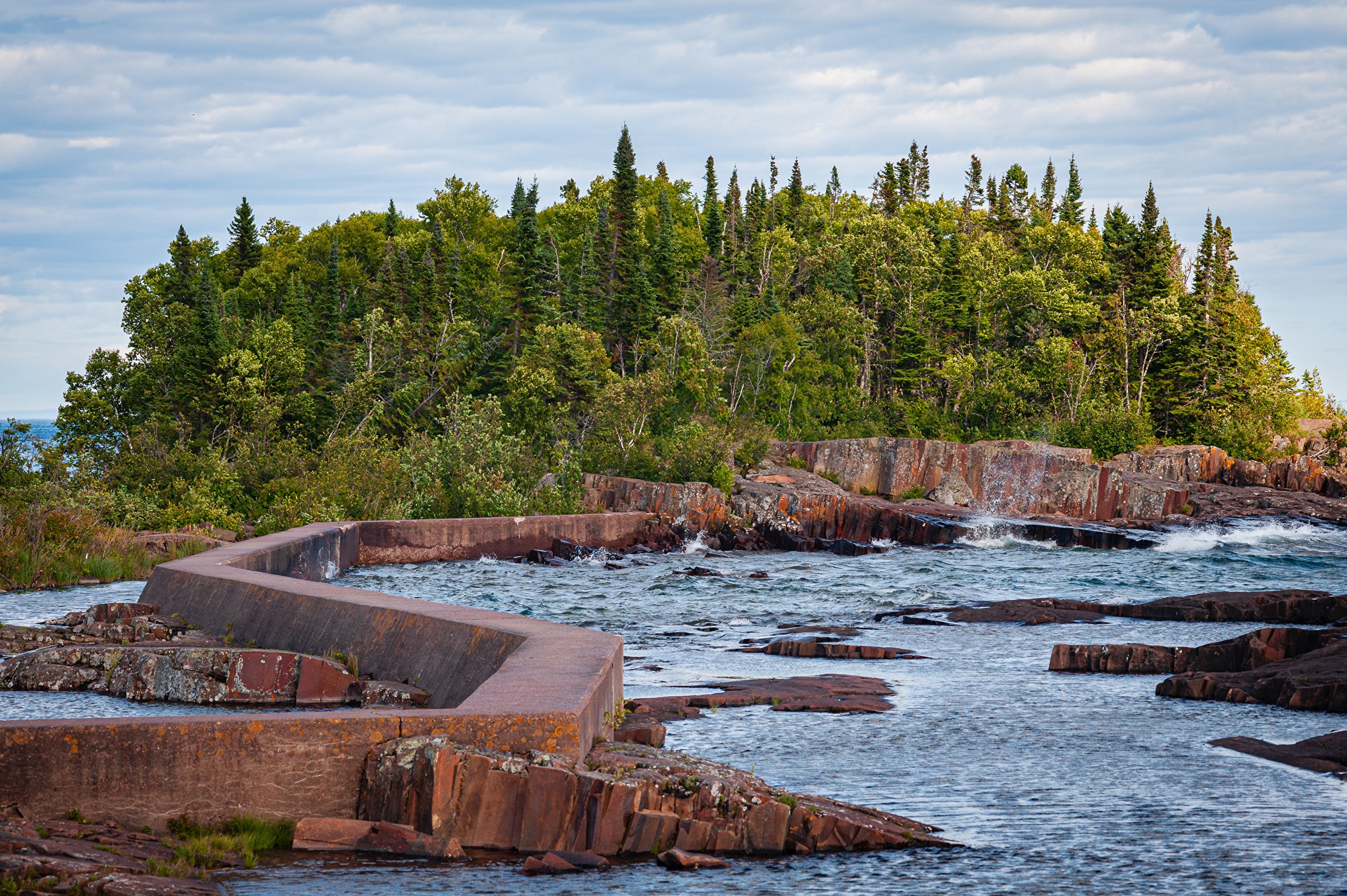 Concrete structure on rocky shore with forest background HD Wallpaper