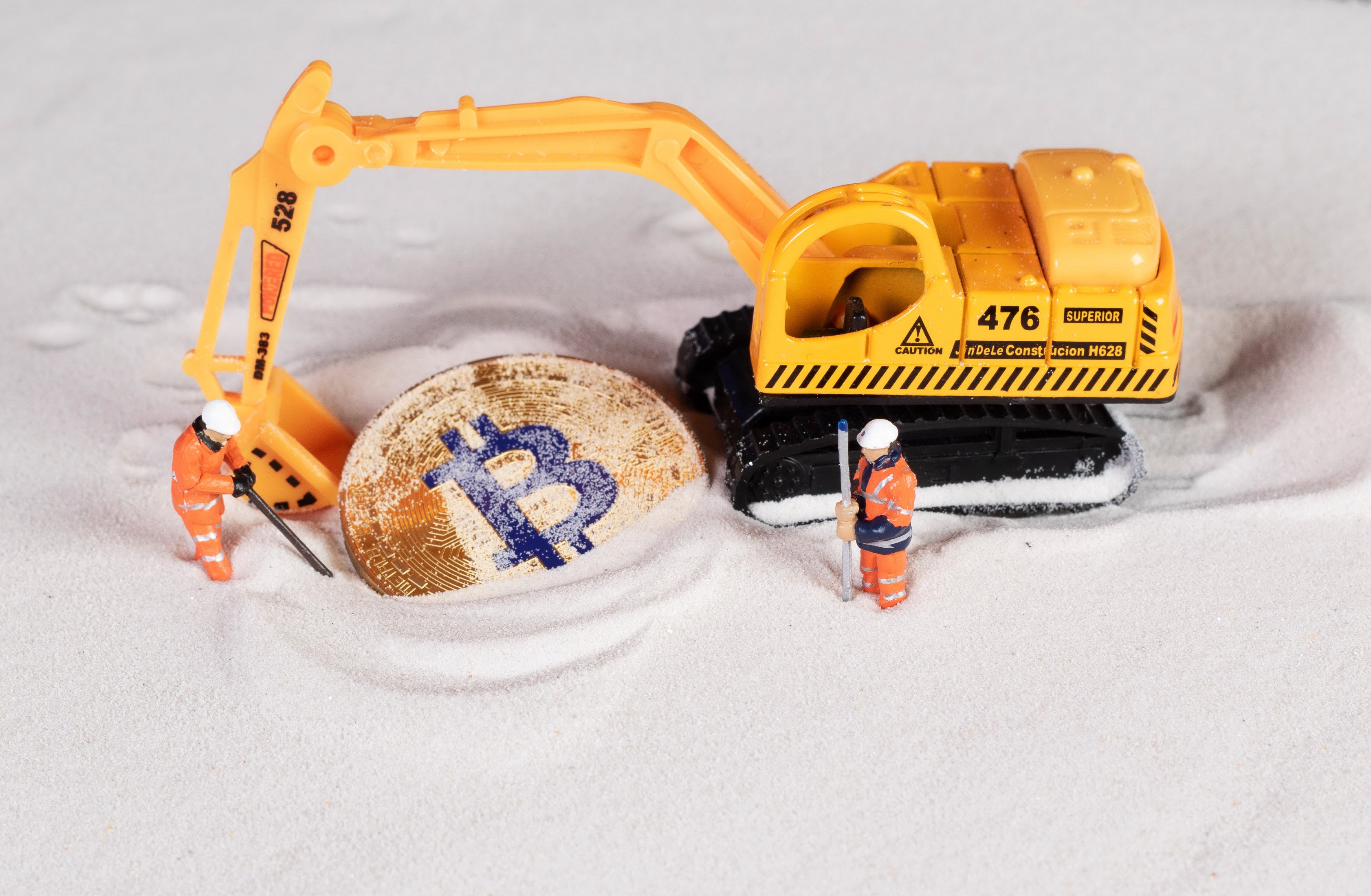 Toy excavator and miners digging for Bitcoin in sand HD Wallpaper