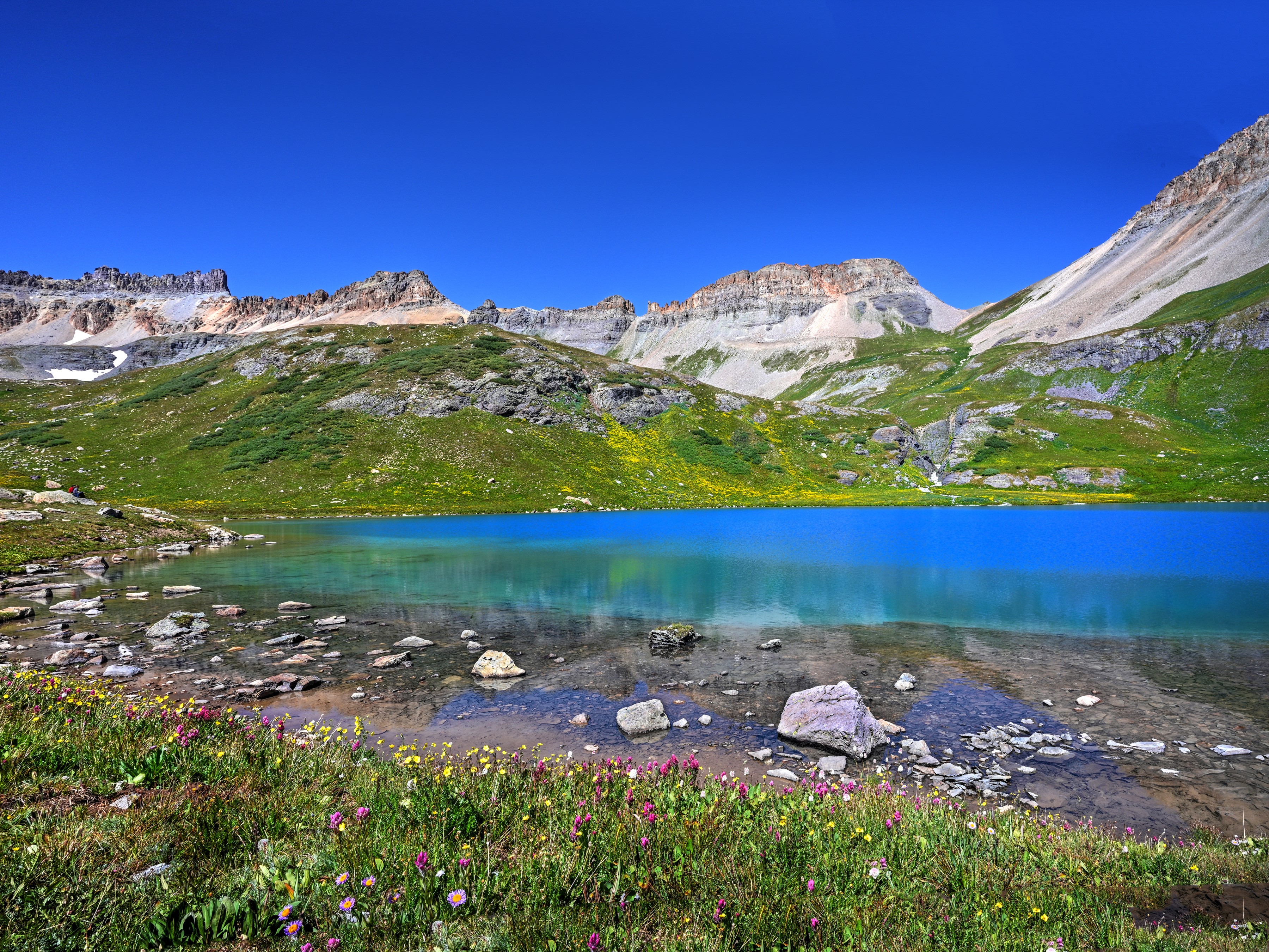 Turquoise lake surrounded by green hills and rocky mountains under a blue sky HD Wallpaper