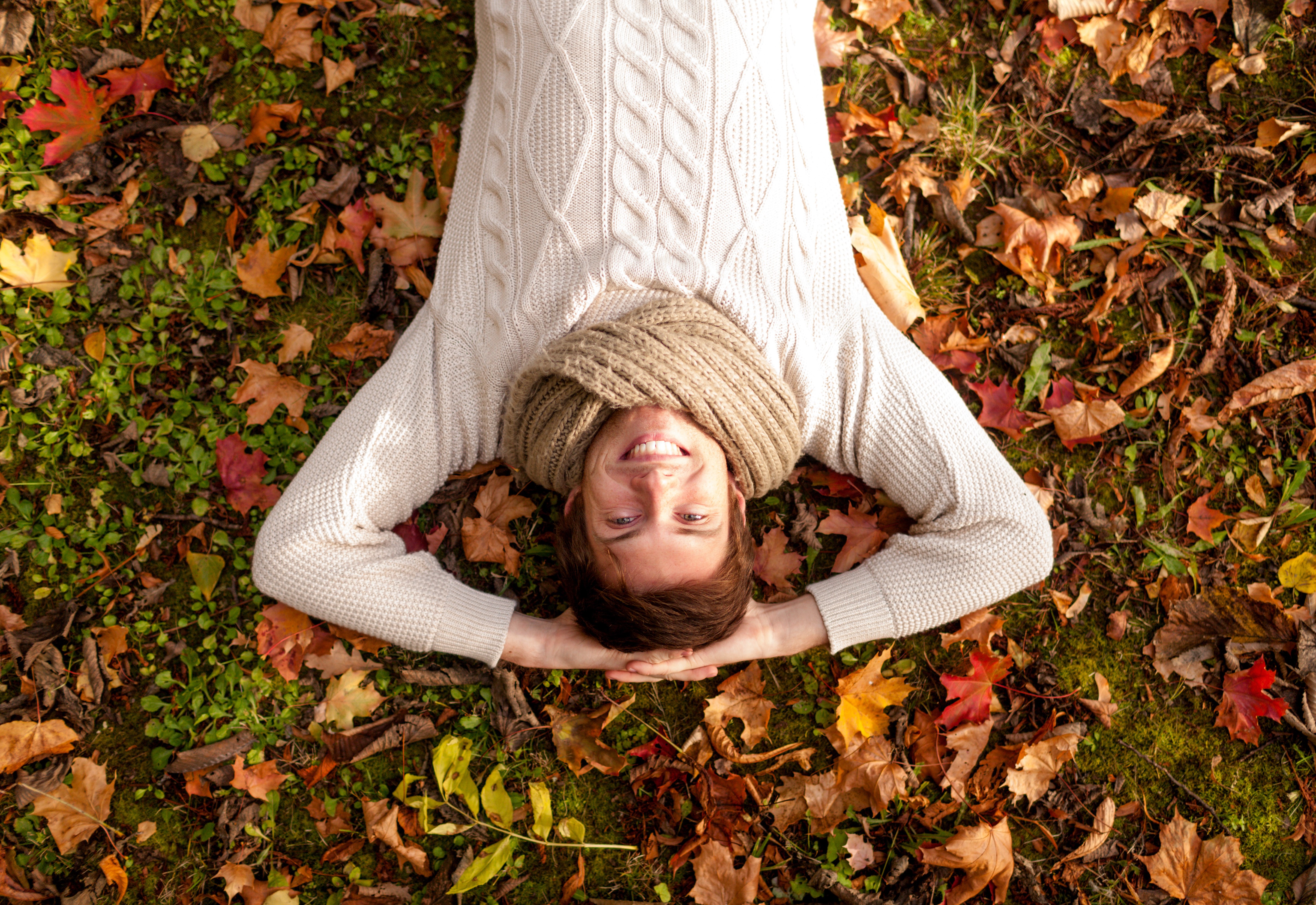 Man lying down in autumn foliage wearing a sweater and scarf HD Wallpaper