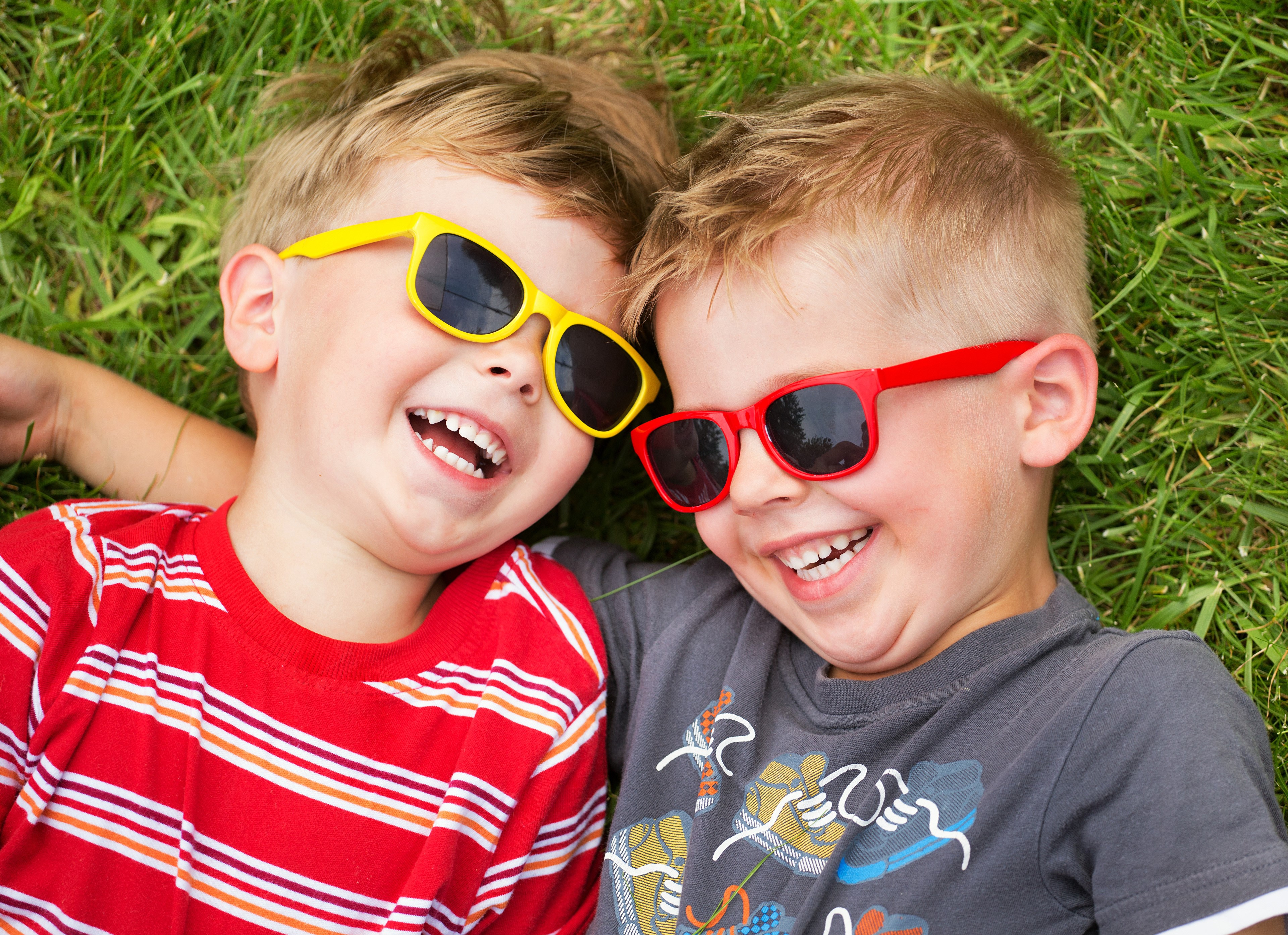 Two boys wearing sunglasses lying on grass HD Wallpaper
