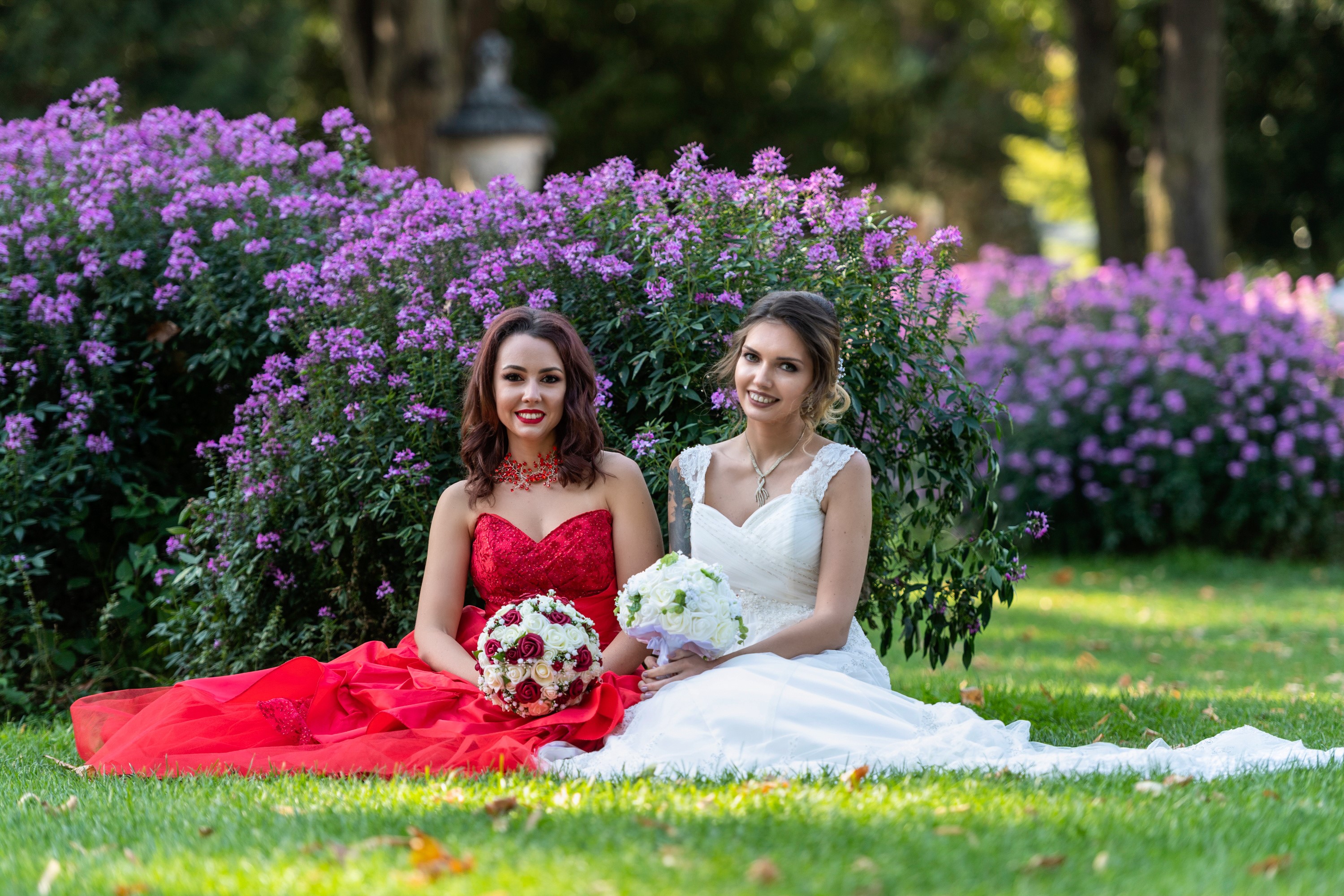 Two women in dresses with bouquets sitting in a garden HD Wallpaper