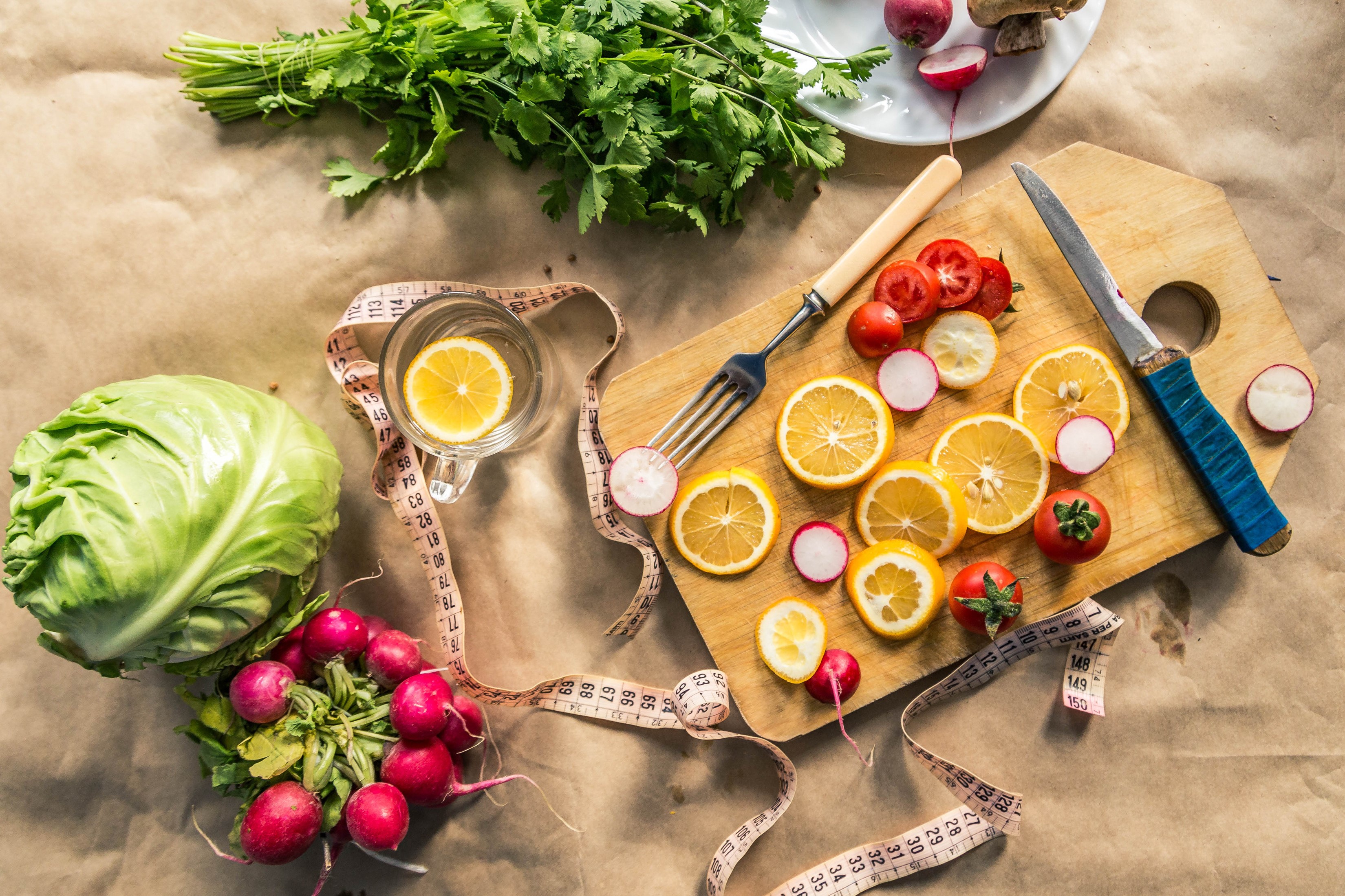 Vegetables, lemons, and radishes on a cutting board with a measuring tape HD Wallpaper