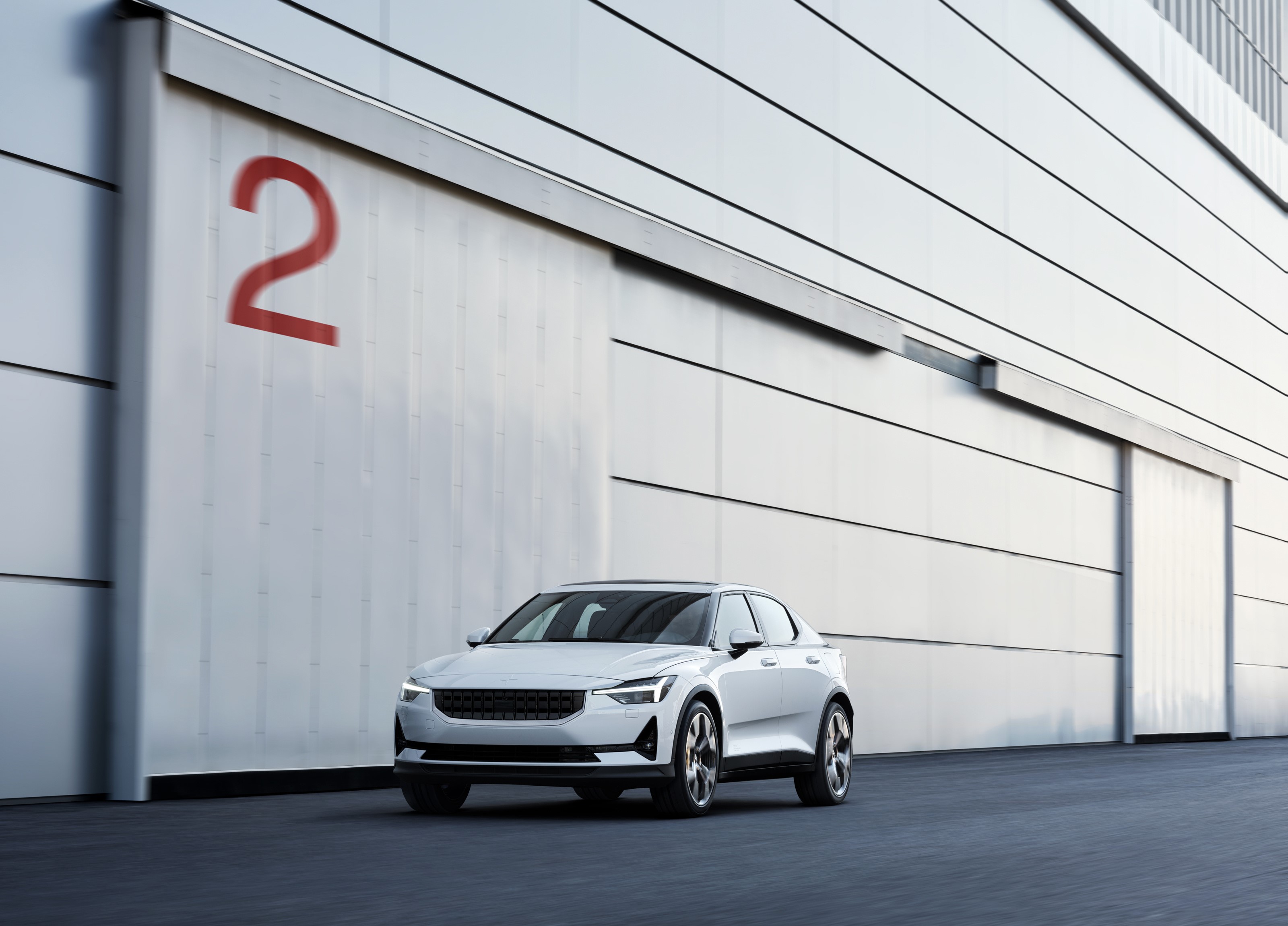 White Polestar 2 parked in front of a building with a large red 2 HD Wallpaper
