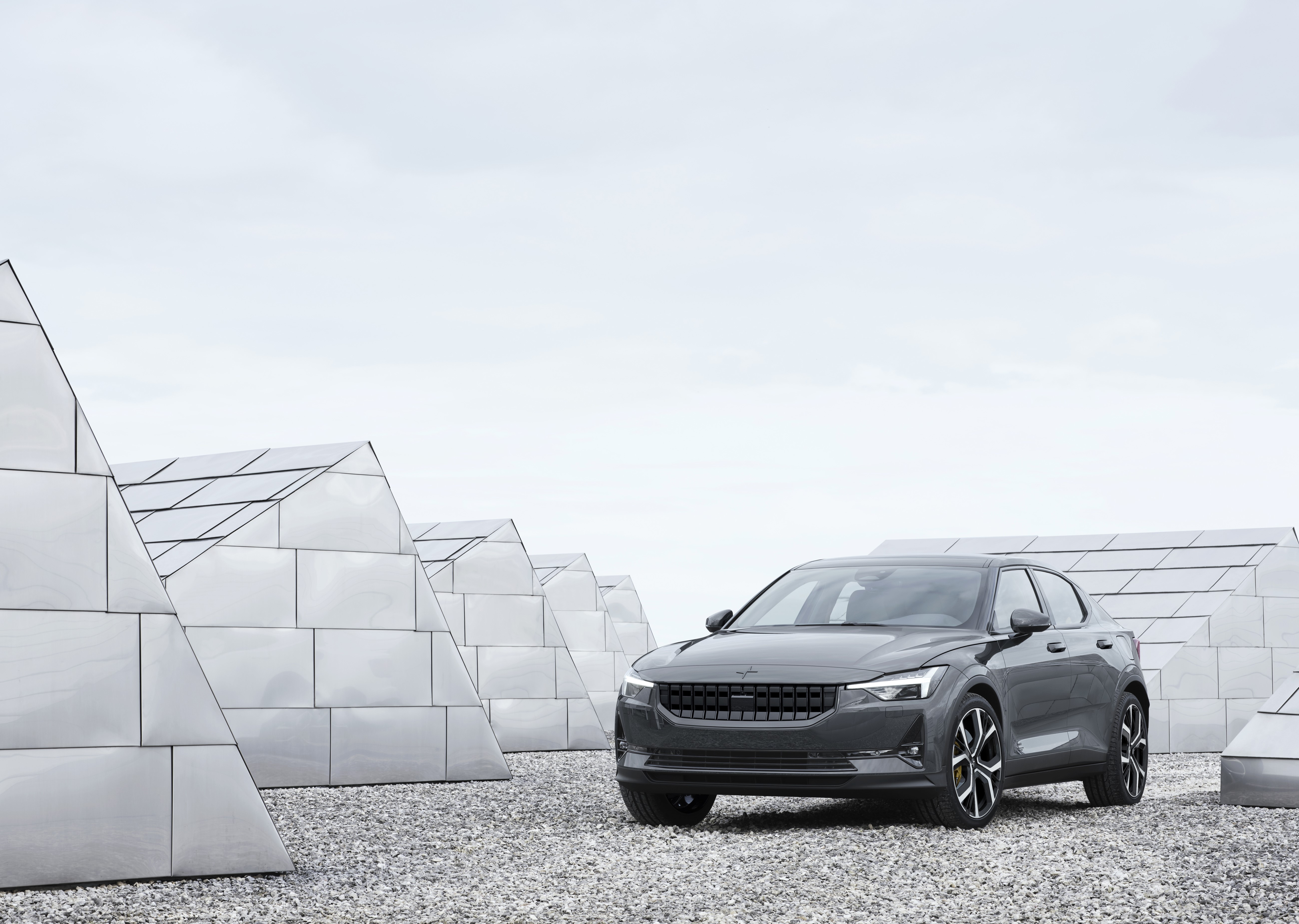 Grey Polestar 2 parked on gravel near modern architecture HD Wallpaper