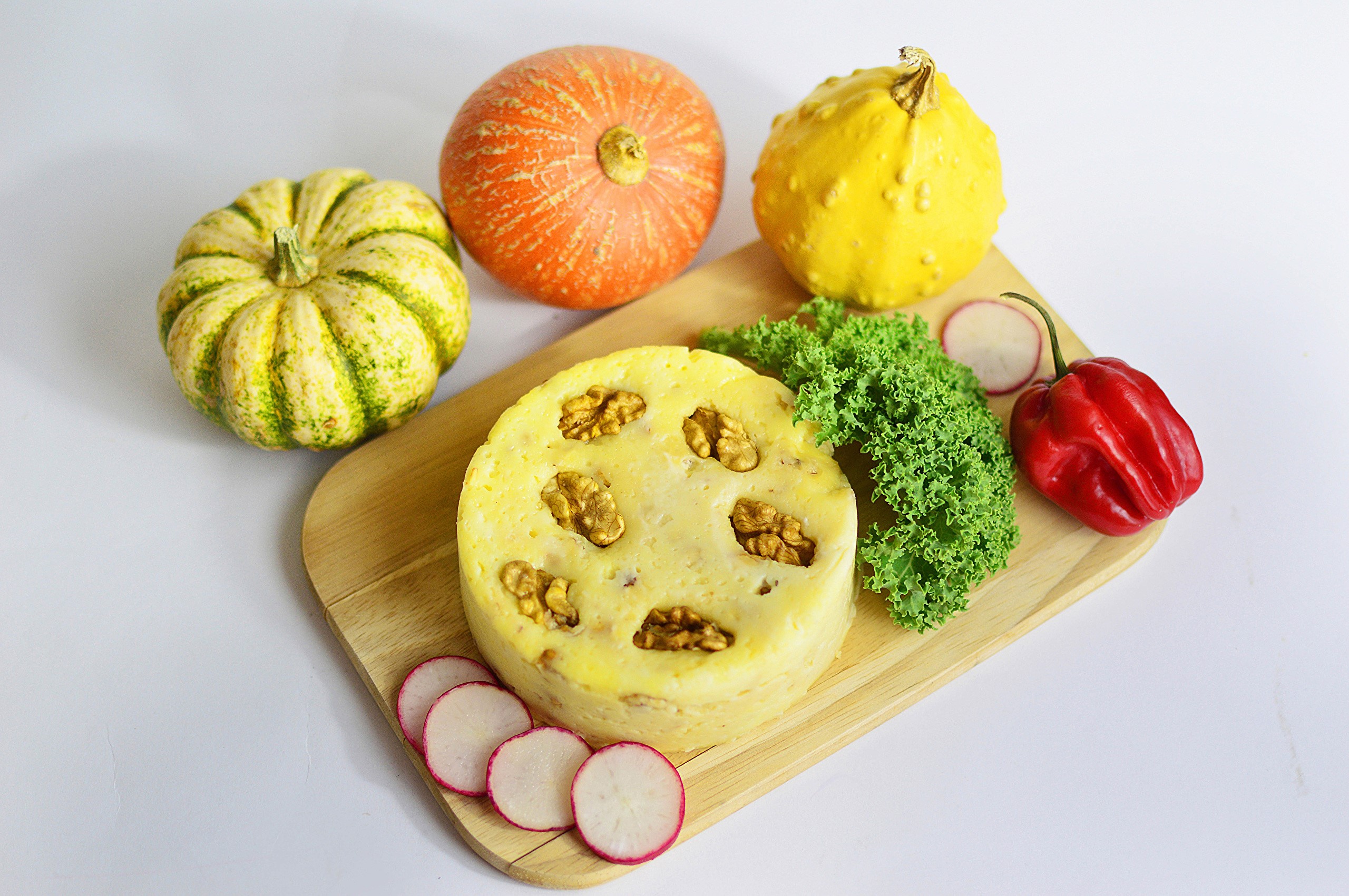 Round pastry with walnuts, pumpkins, bell pepper, and radishes on a cutting board HD Wallpaper