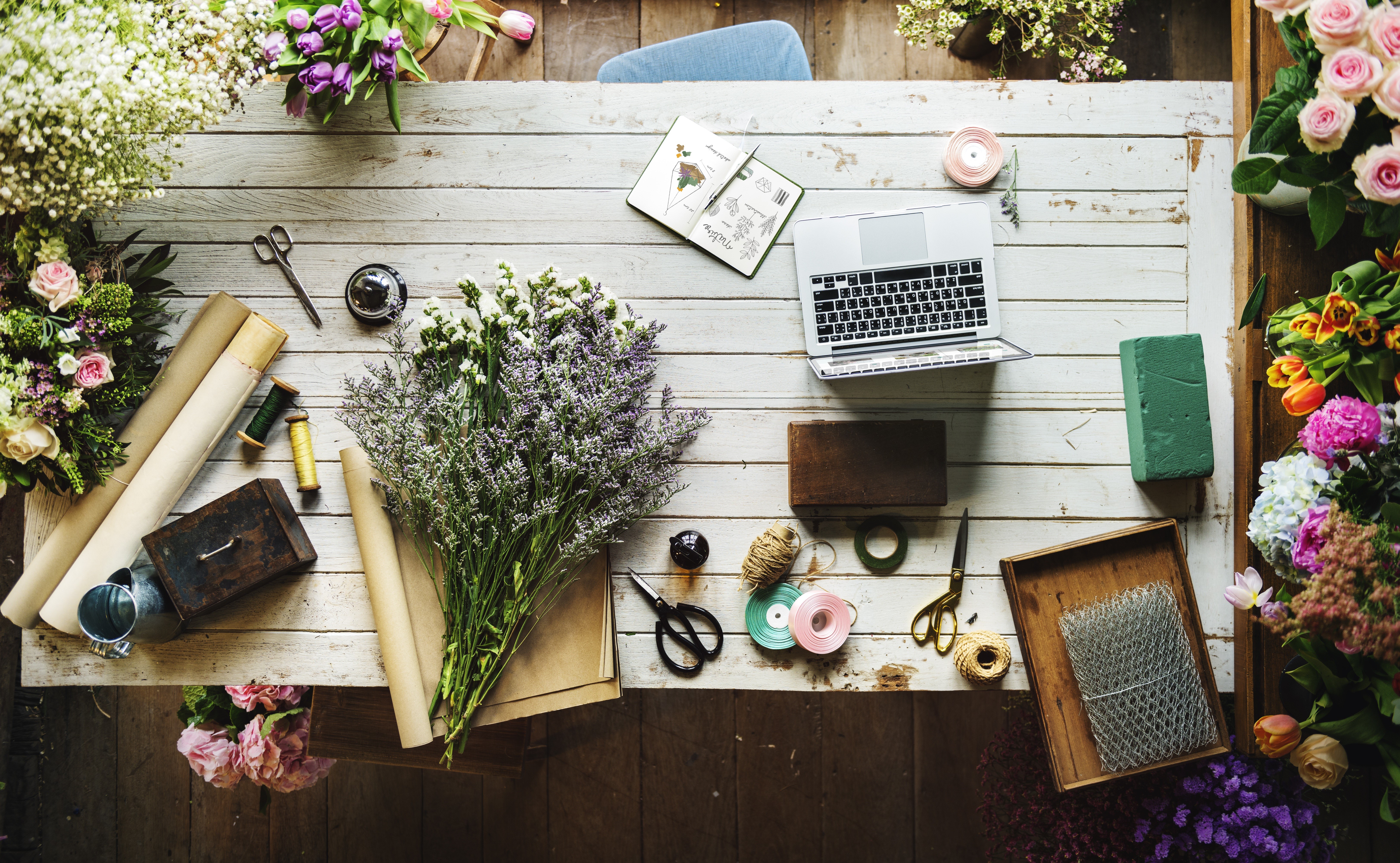Florist's table with laptop, flowers, and supplies HD Wallpaper