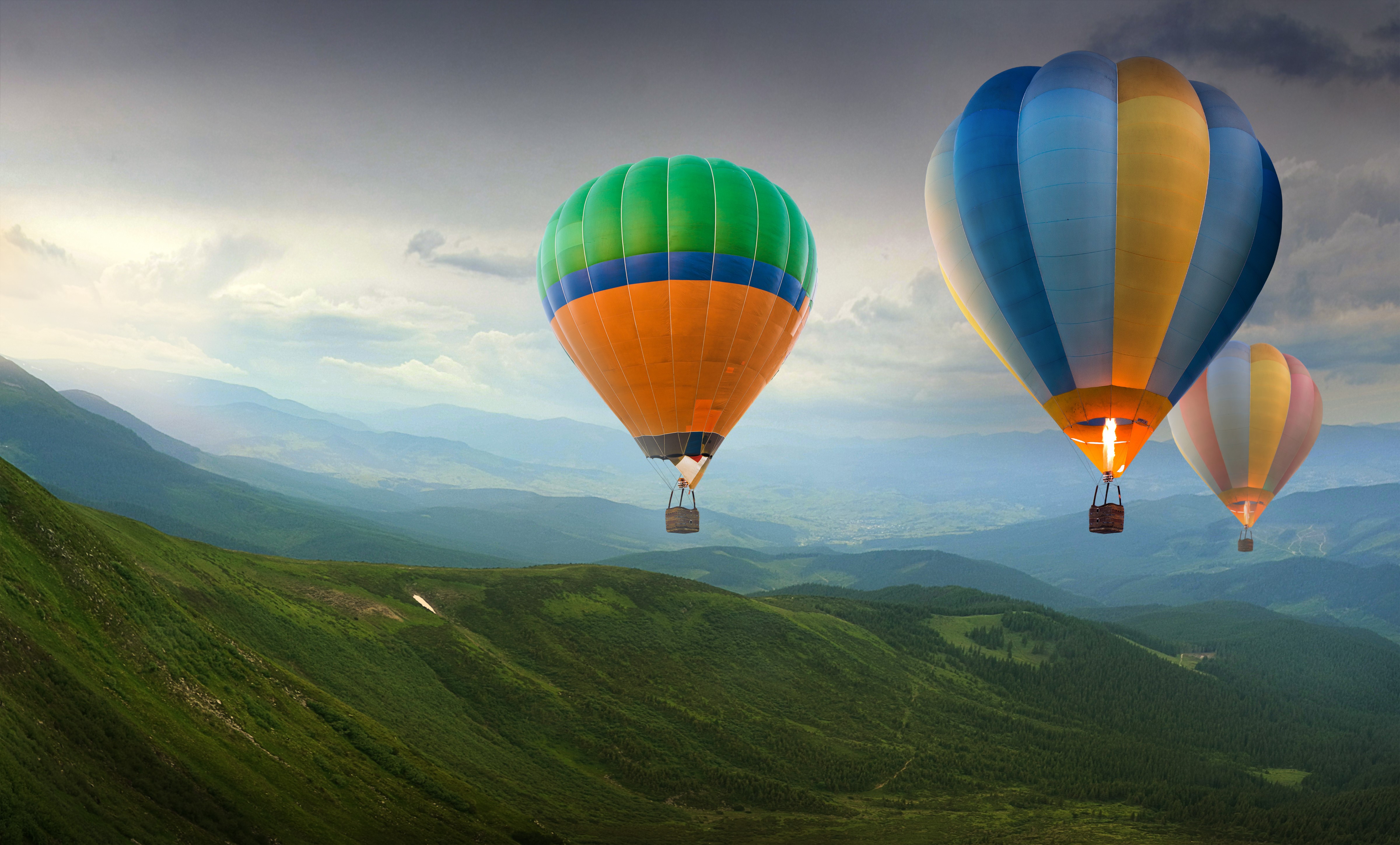 Hot air balloons flying over green hills HD Wallpaper