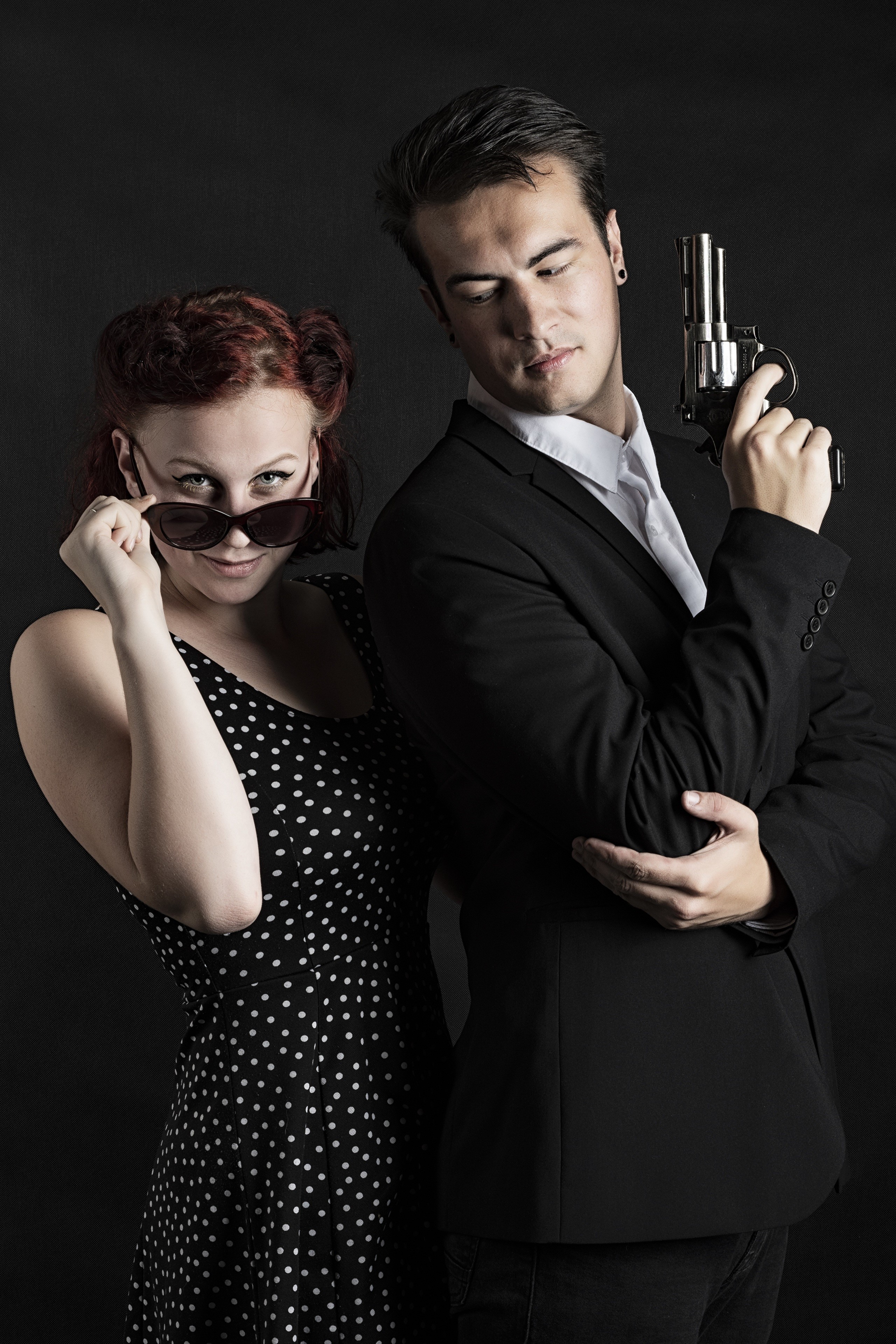 Man in suit holding a pistol with a woman in a polka dot dress HD Phone Wallpaper