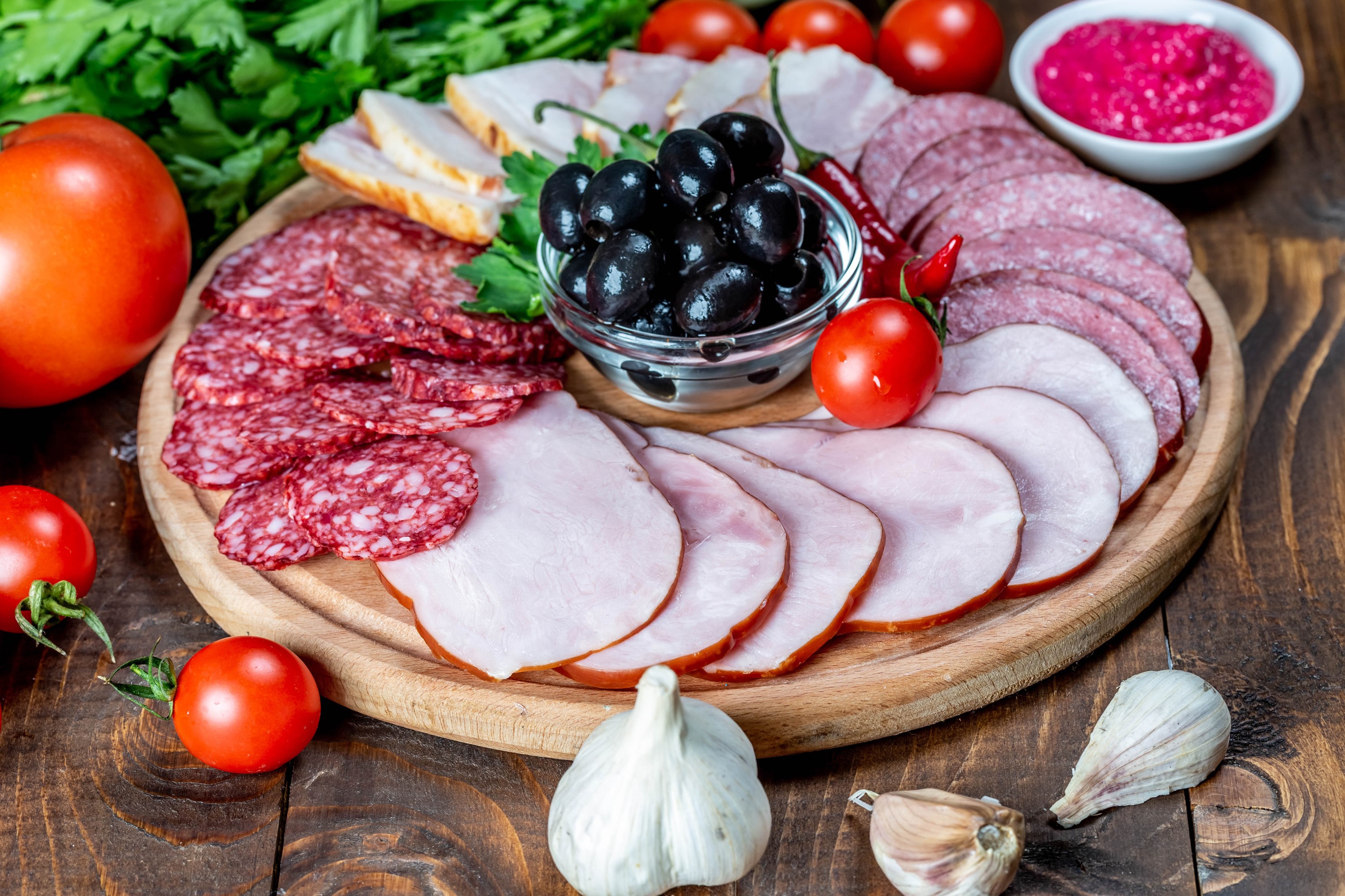 Charcuterie board with assorted meats, olives, tomatoes, and garlic HD Wallpaper