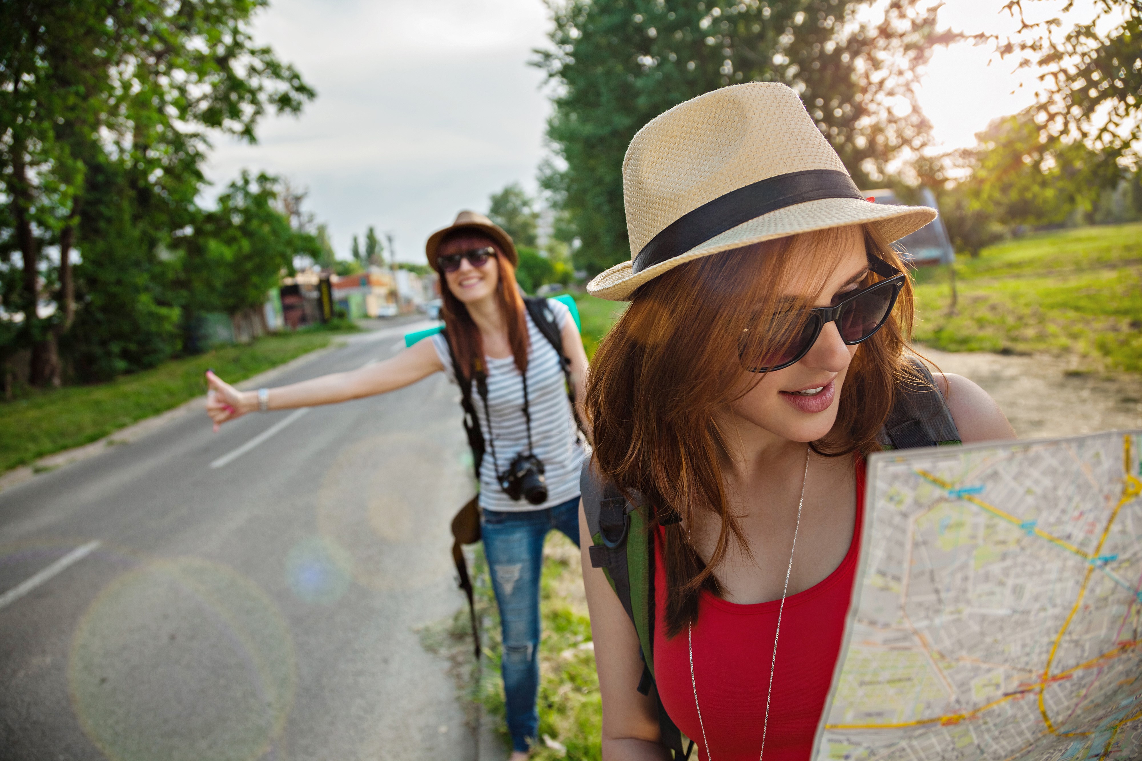 Two tourists hitchhiking on a road with a map HD Wallpaper