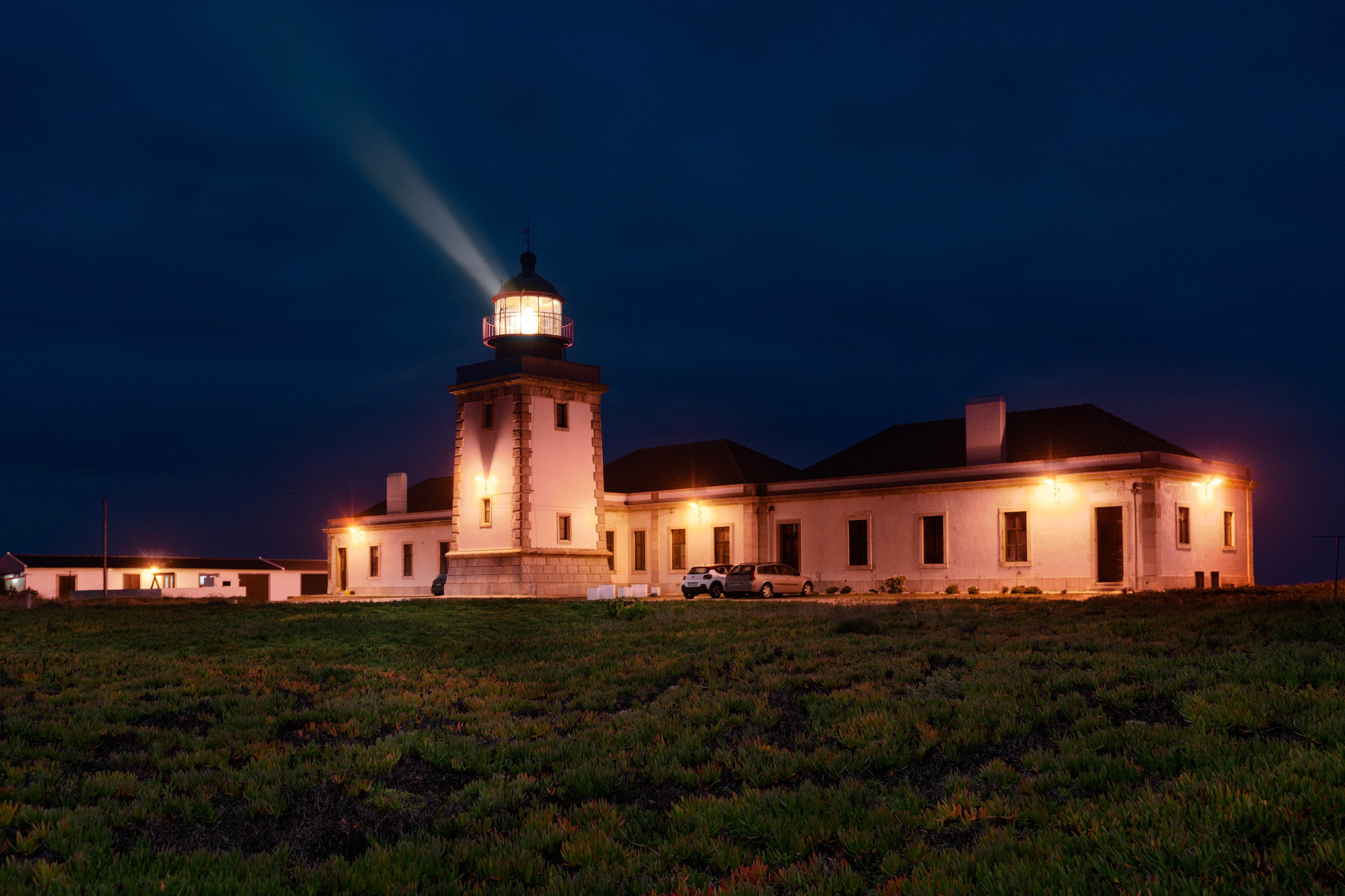 Lighthouse at night with light beam and buildings in Carrapateira, Portugal HD Wallpaper