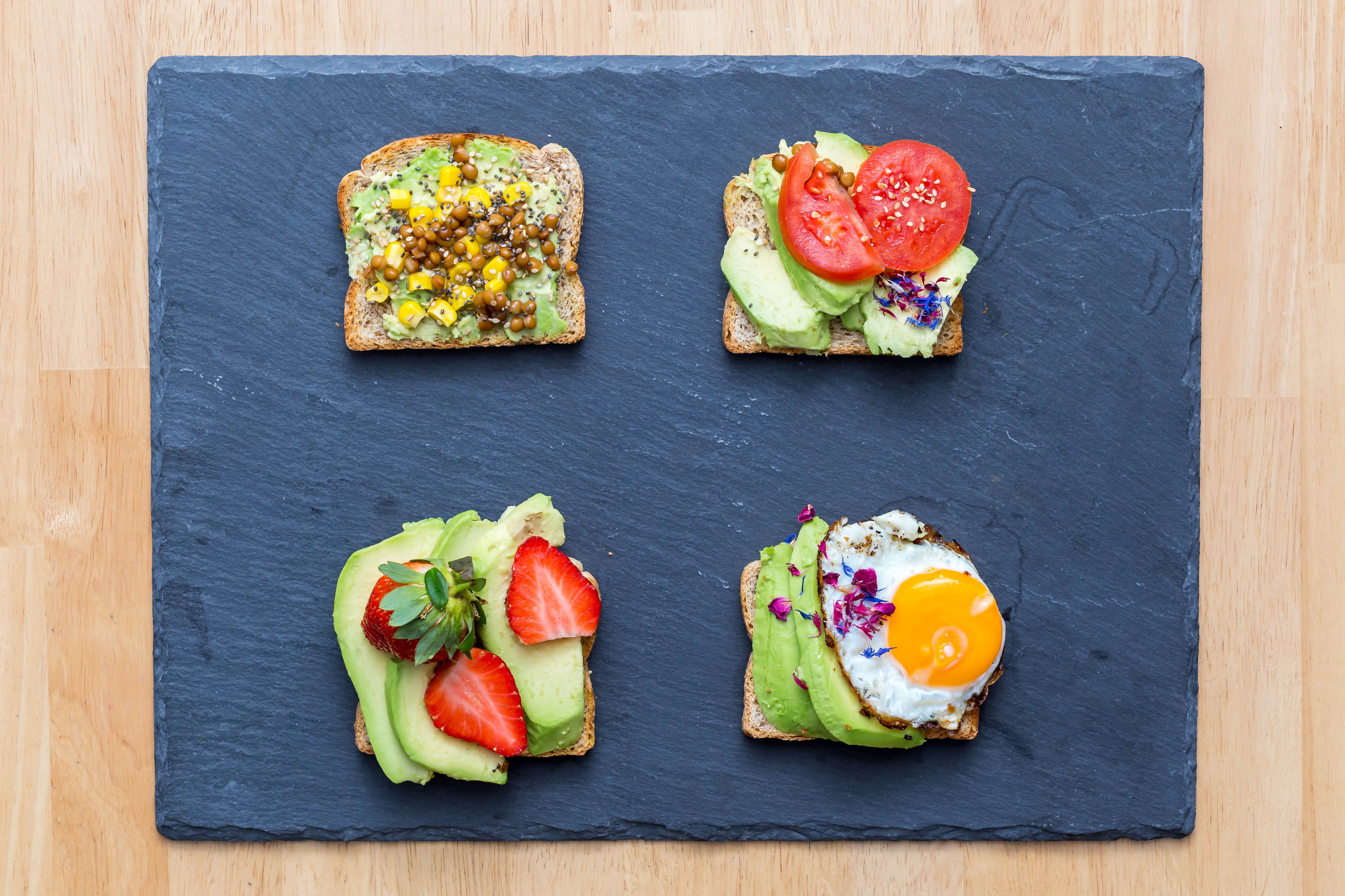 Four avocado toasts with toppings on a slate board HD Wallpaper