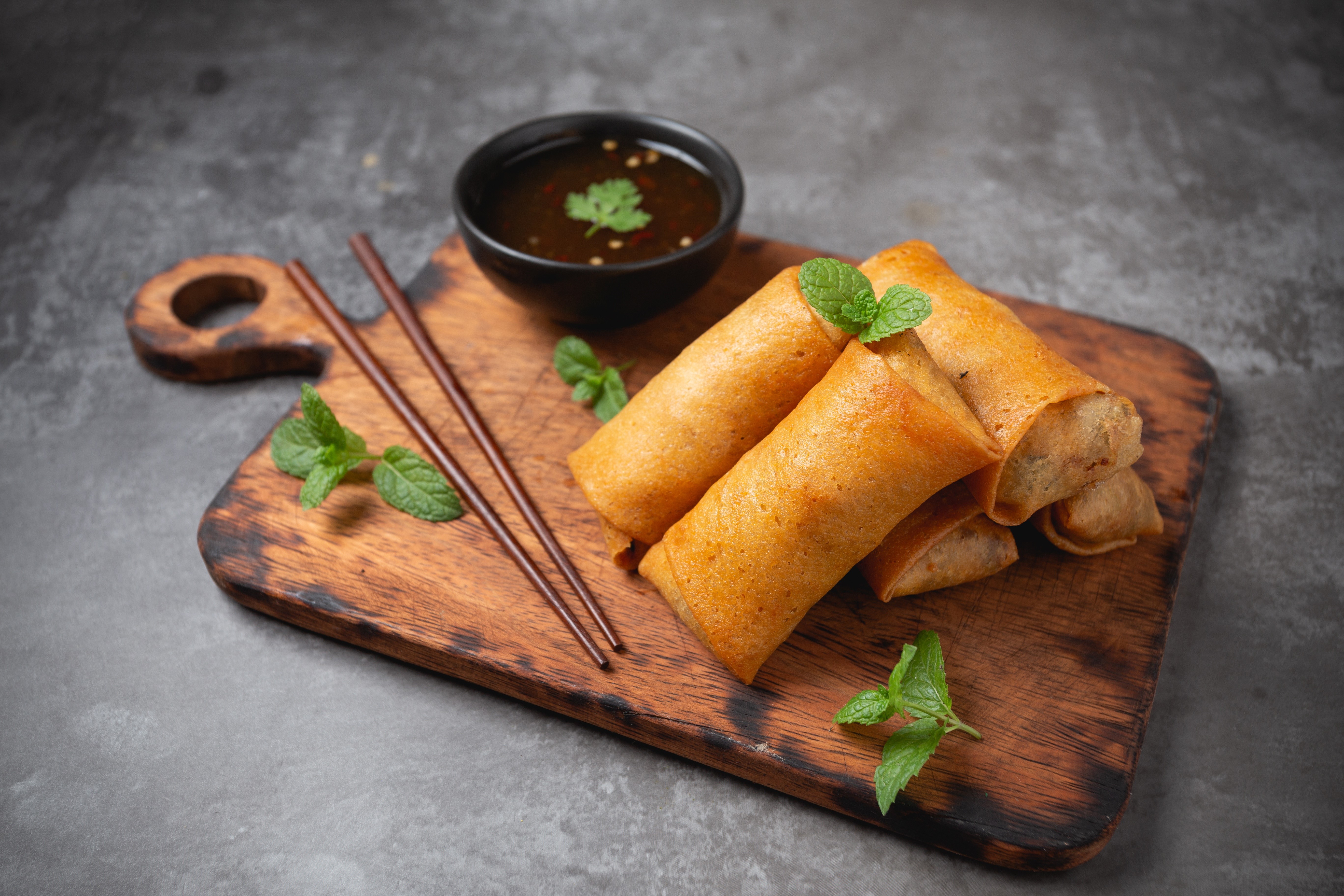 Spring rolls with dipping sauce and chopsticks on a cutting board HD Wallpaper
