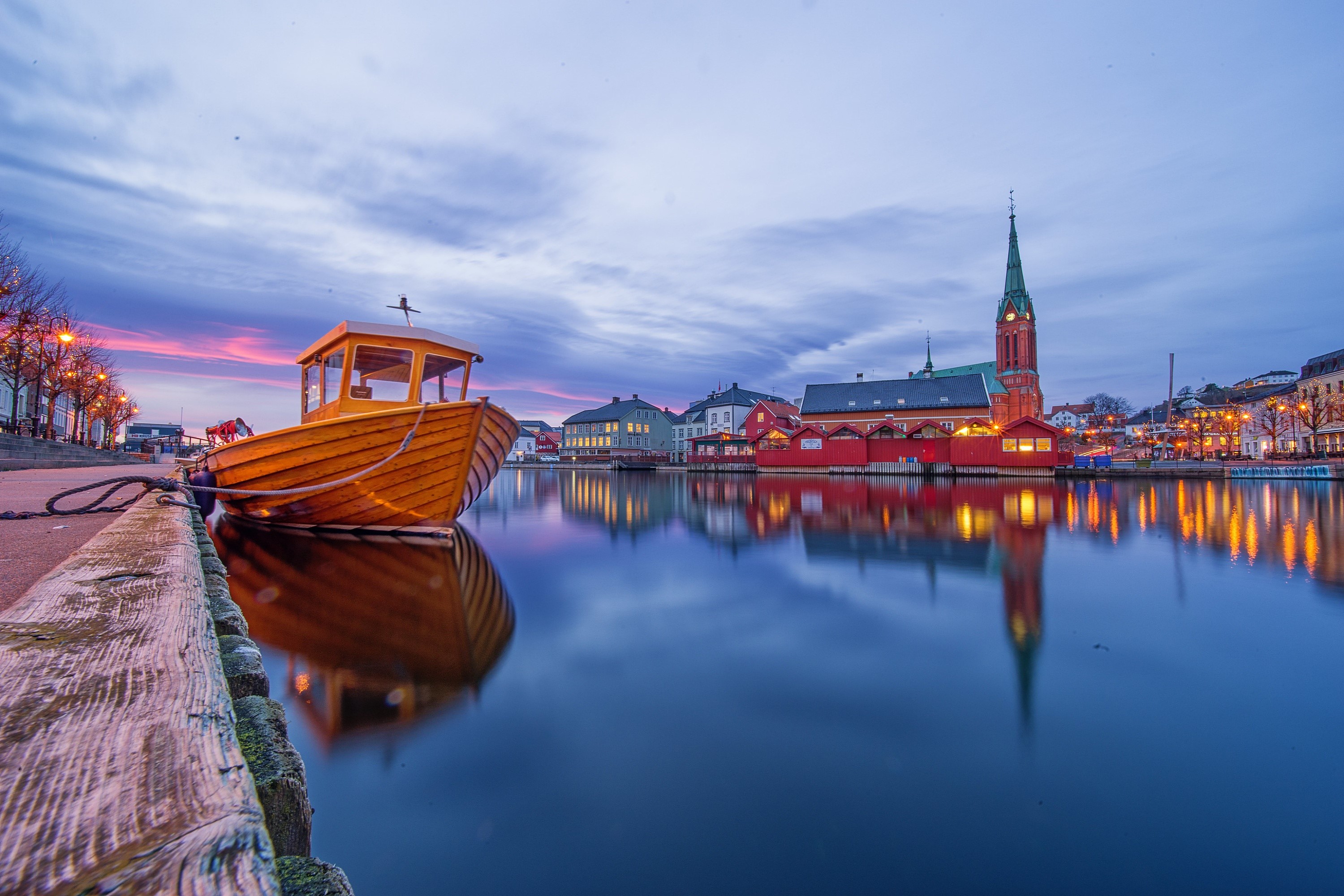 Boat docked by canal with church in Arendal, Norway at dusk HD Wallpaper