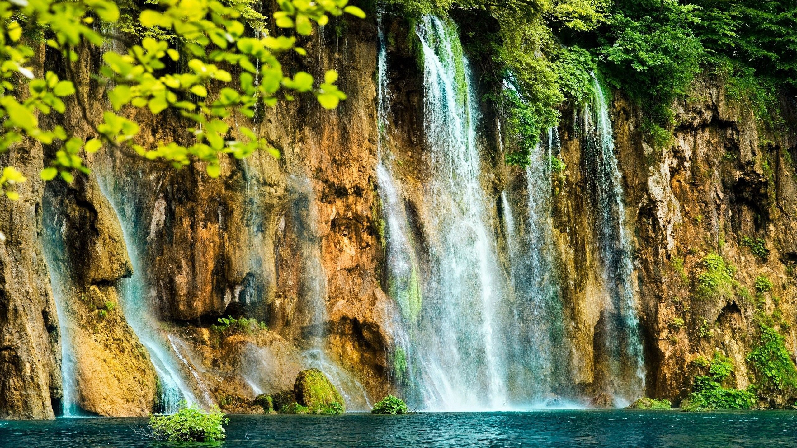 Waterfall cascading down a rocky cliff into a blue lake HD Wallpaper