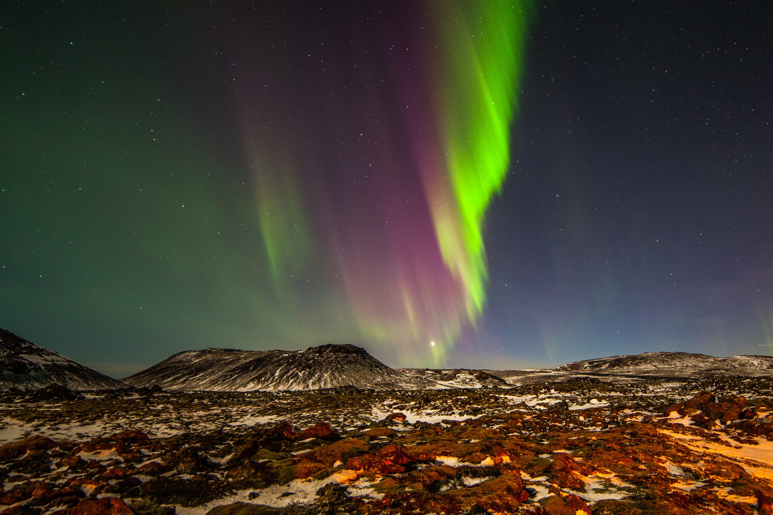 Aurora Borealis over a snowy, rocky landscape HD Wallpaper