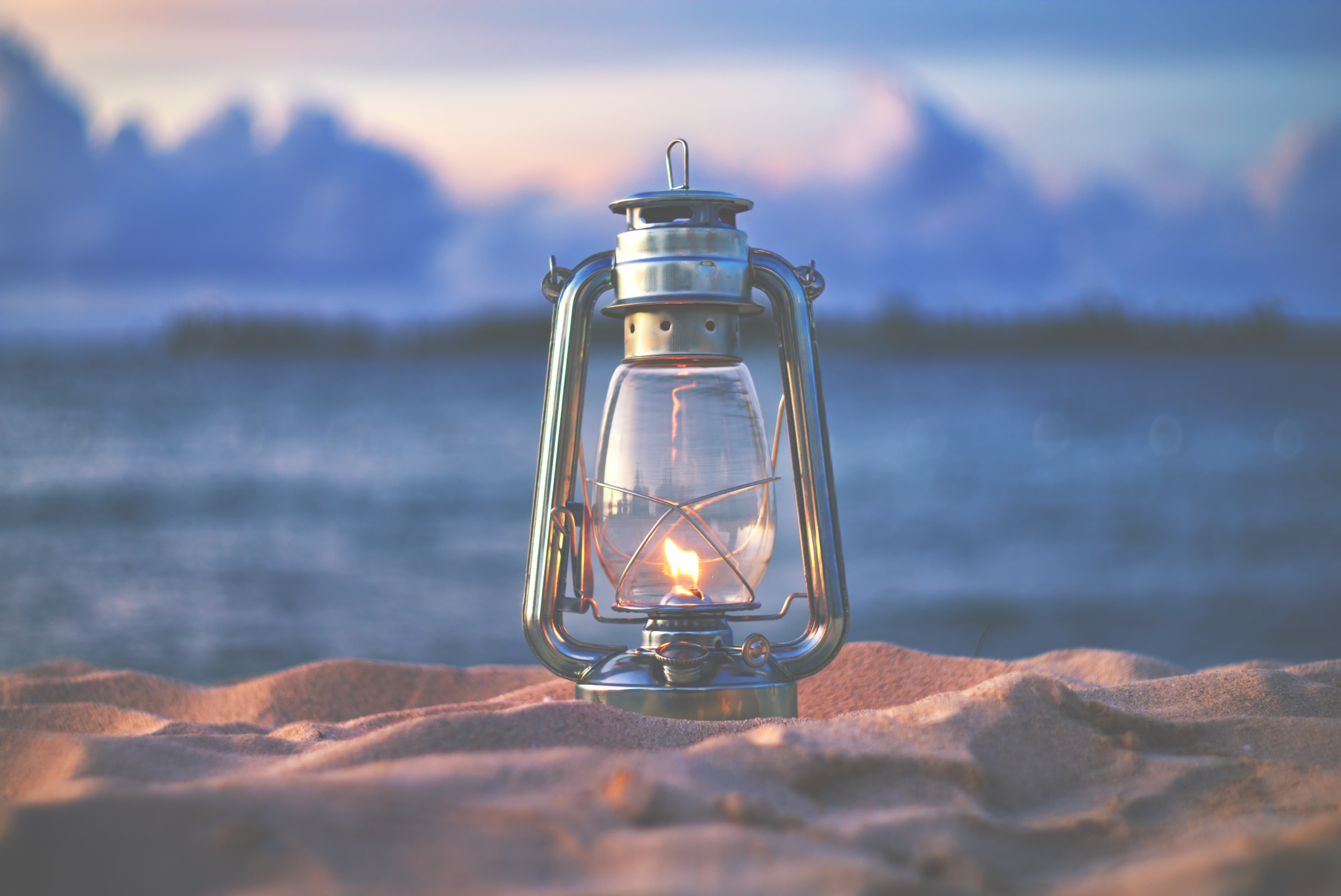Kerosene lamp with fire on sand near water HD Wallpaper