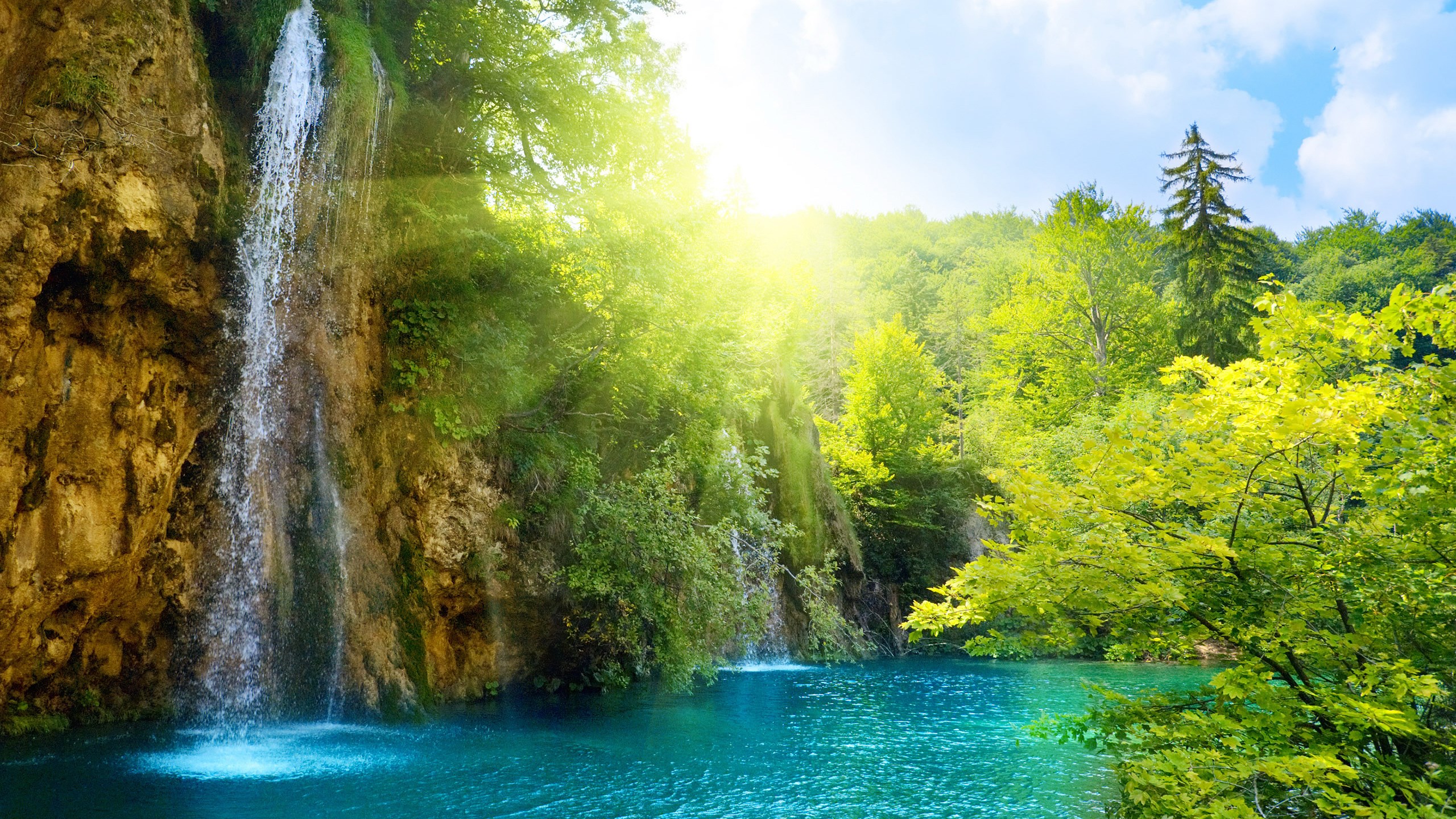 Waterfall cascading into a turquoise lake surrounded by lush green forest HD Wallpaper