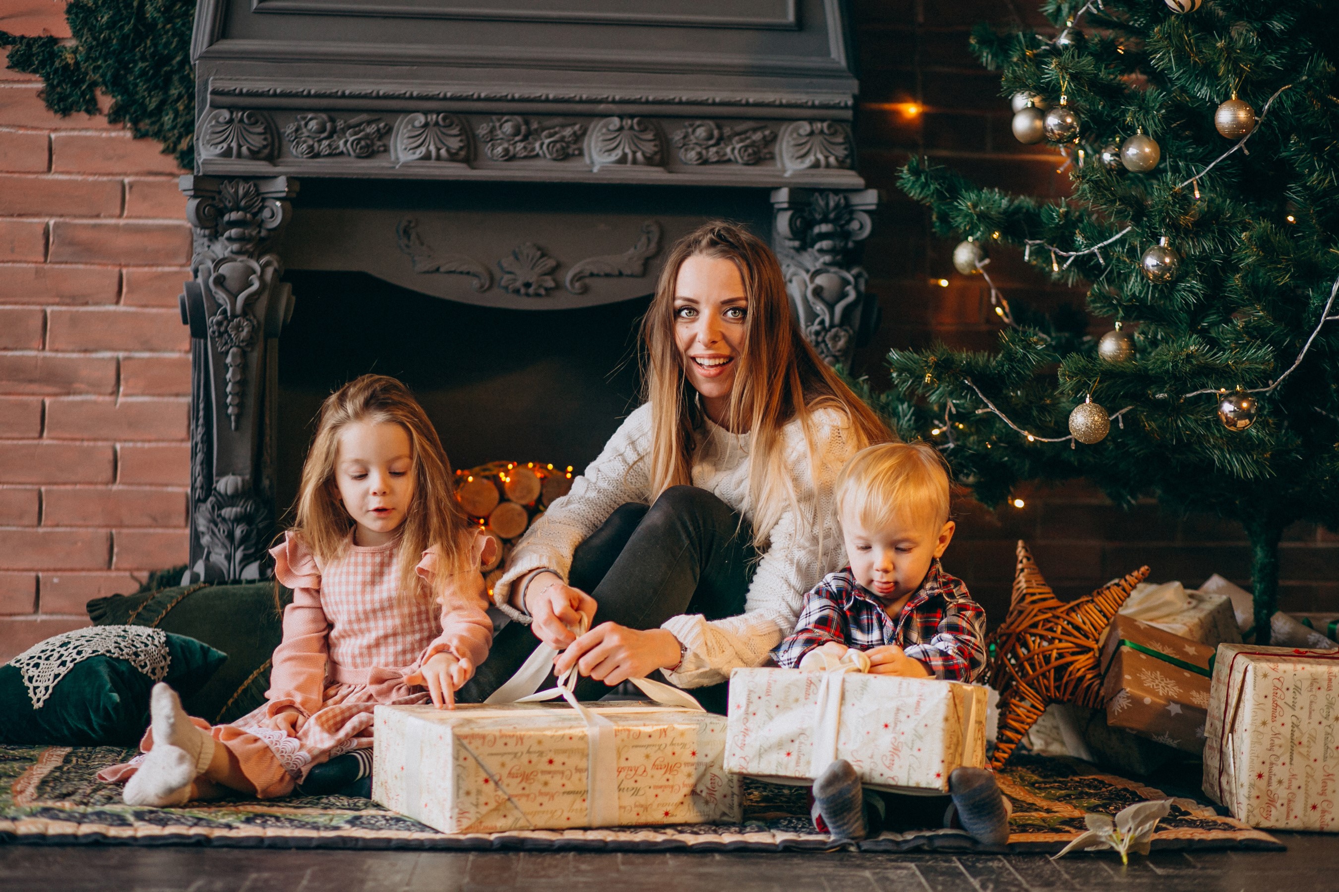 Mother and children opening Christmas gifts by the fireplace and tree HD Wallpaper
