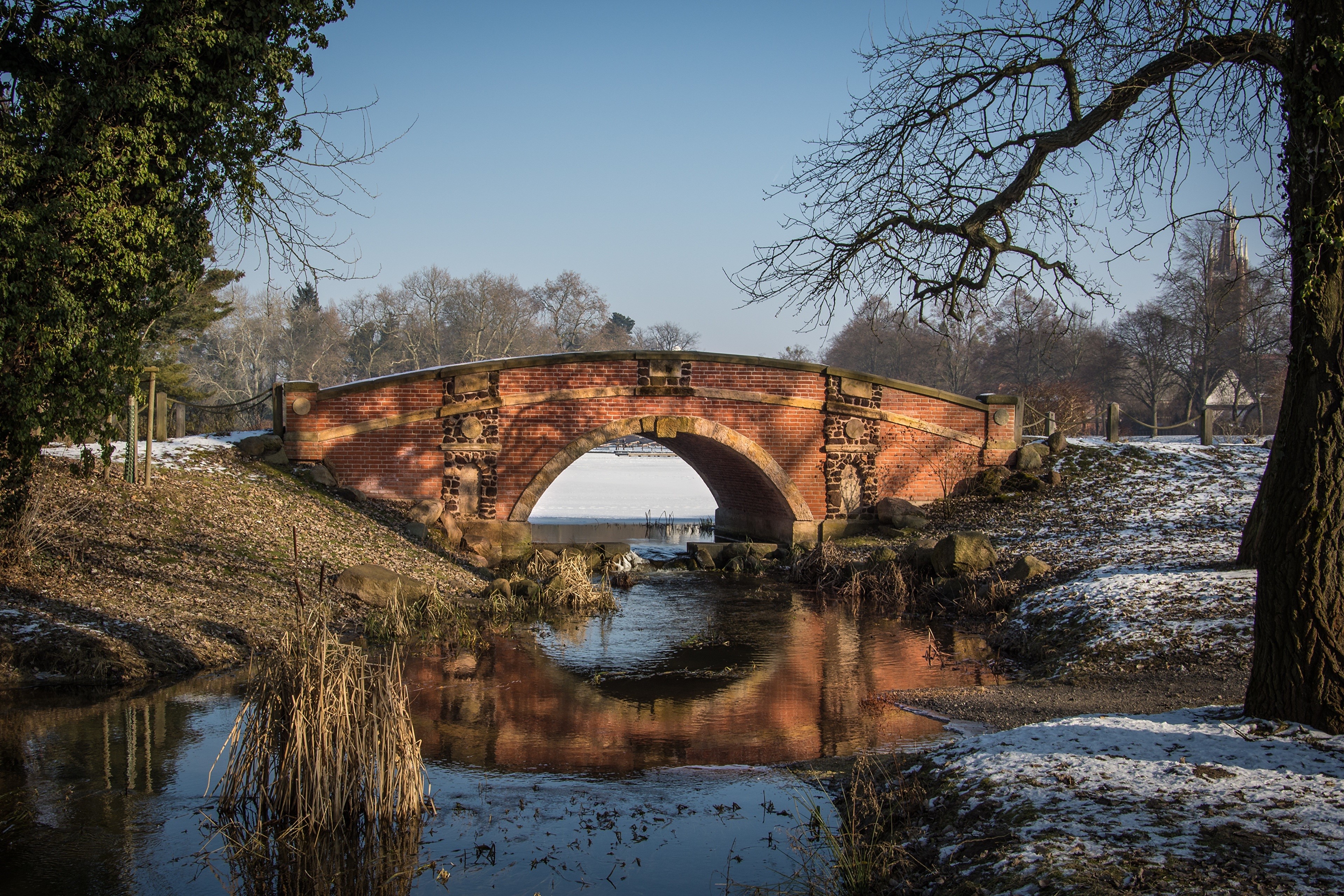 Brick bridge over a frozen stream in a park during winter HD Wallpaper