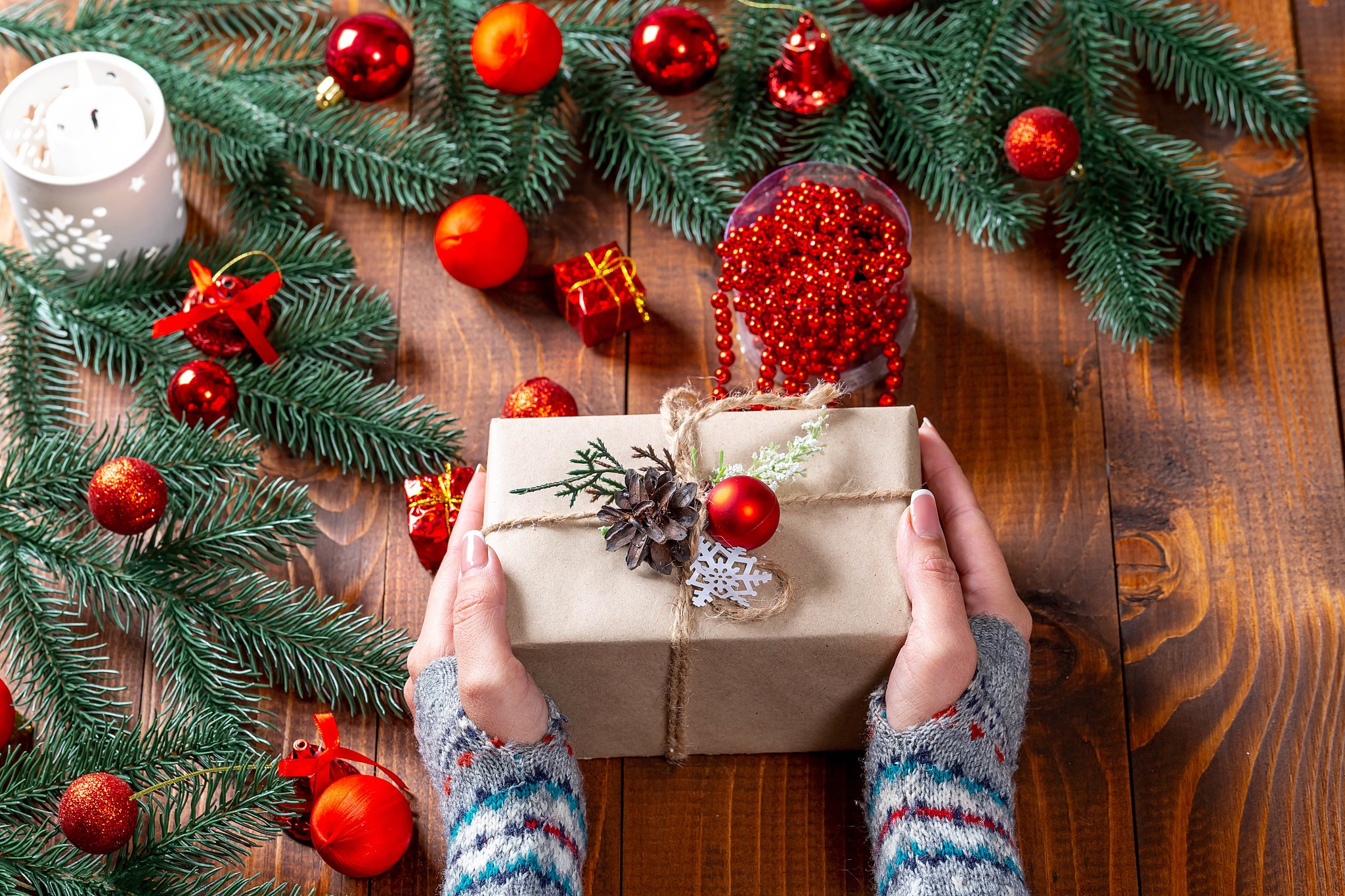 Hands holding a Christmas gift surrounded by decorations HD Wallpaper