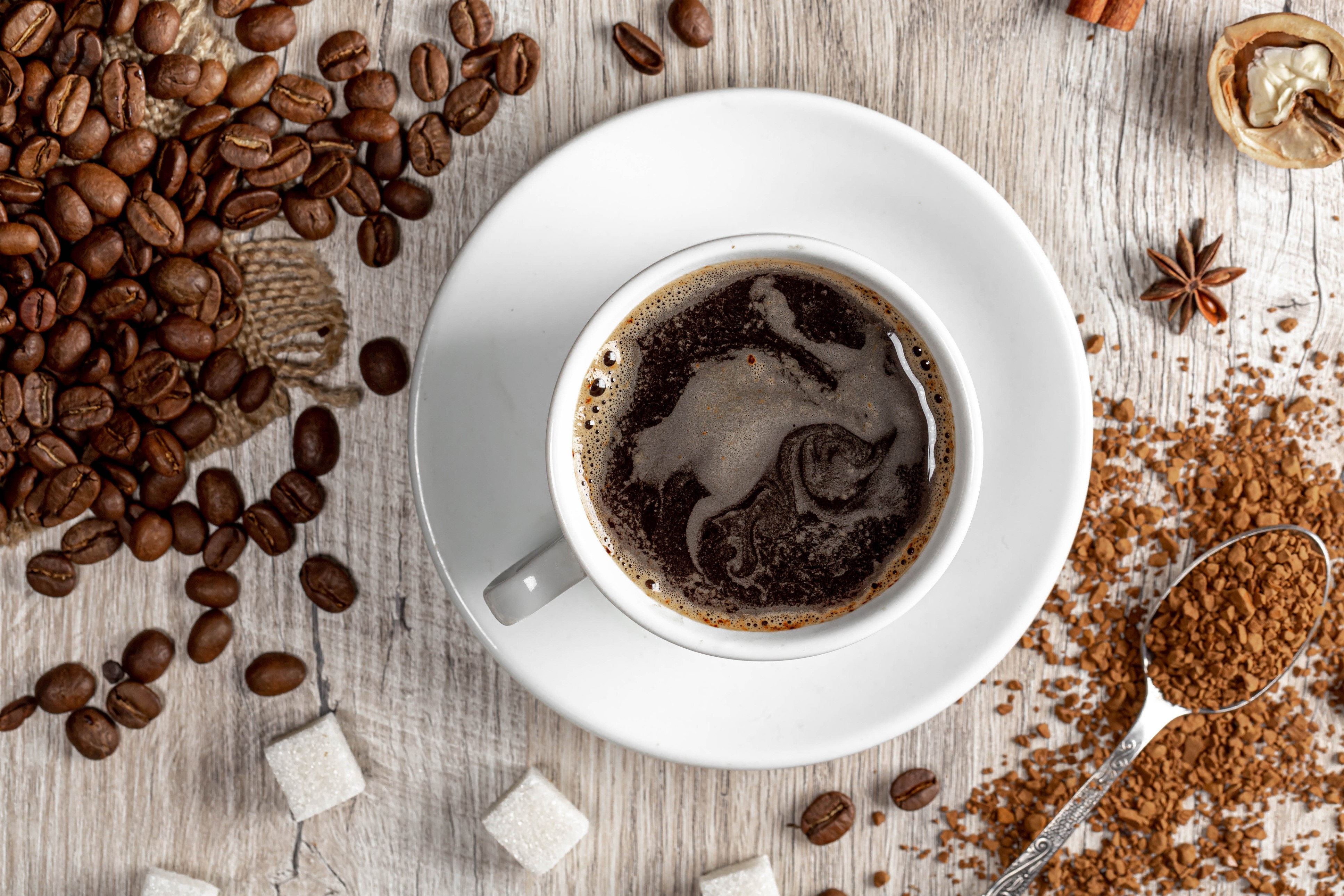 Coffee beans, cup of coffee, sugar cubes, and spices on wood HD Wallpaper