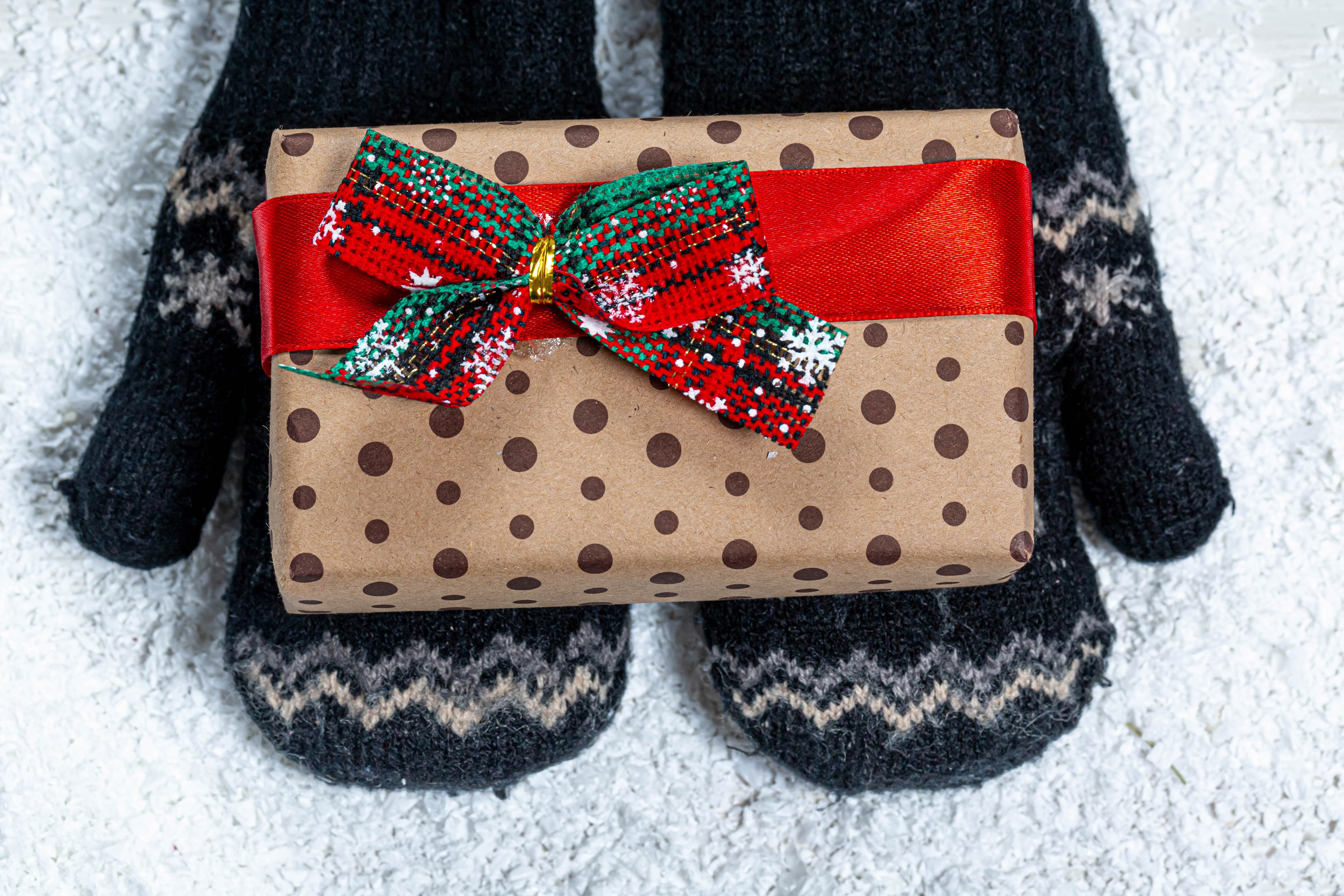 Christmas gift wrapped in brown paper with polka dots held by mittens HD Wallpaper