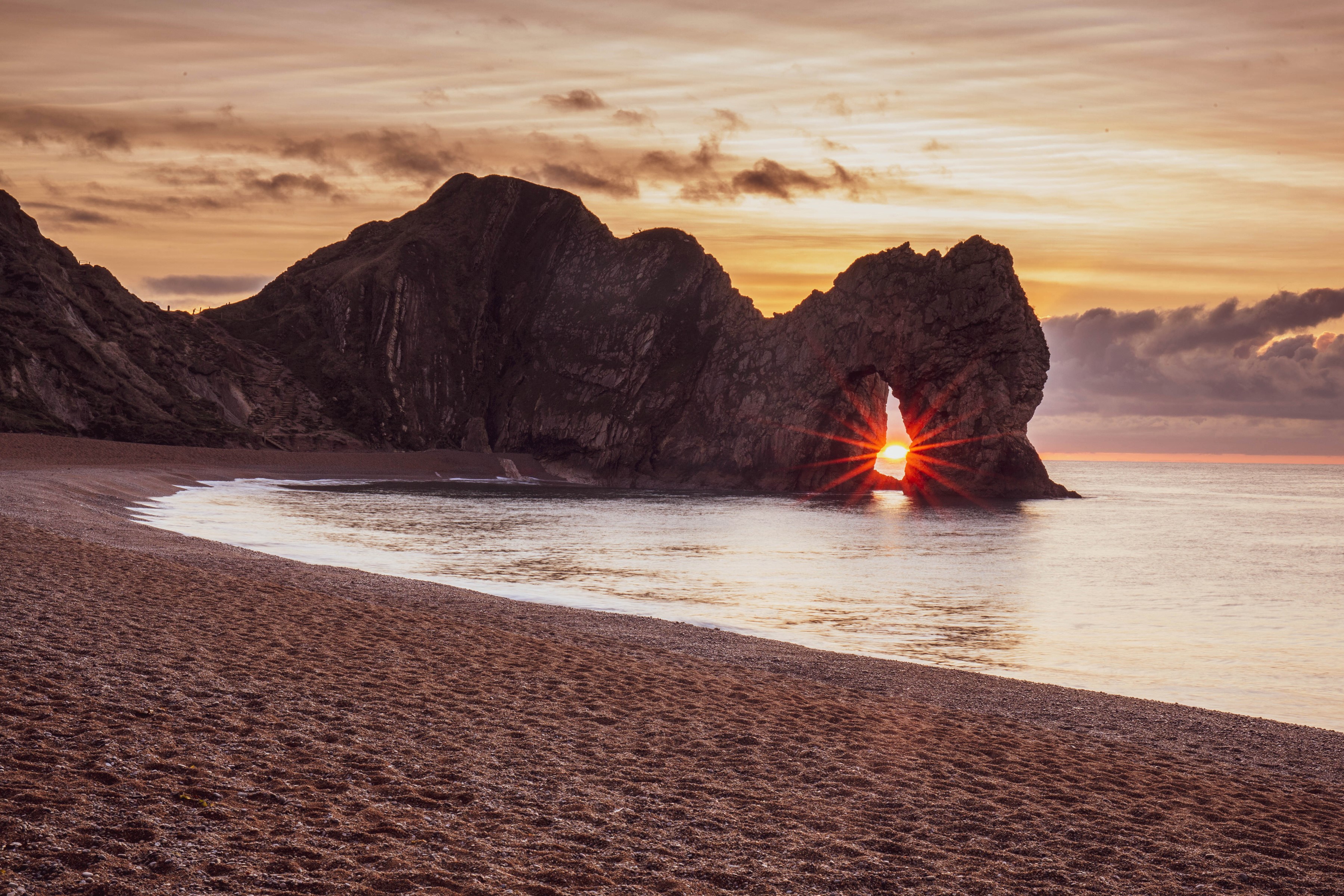Sunrise through Durdle Door arch on a pebble beach HD Wallpaper