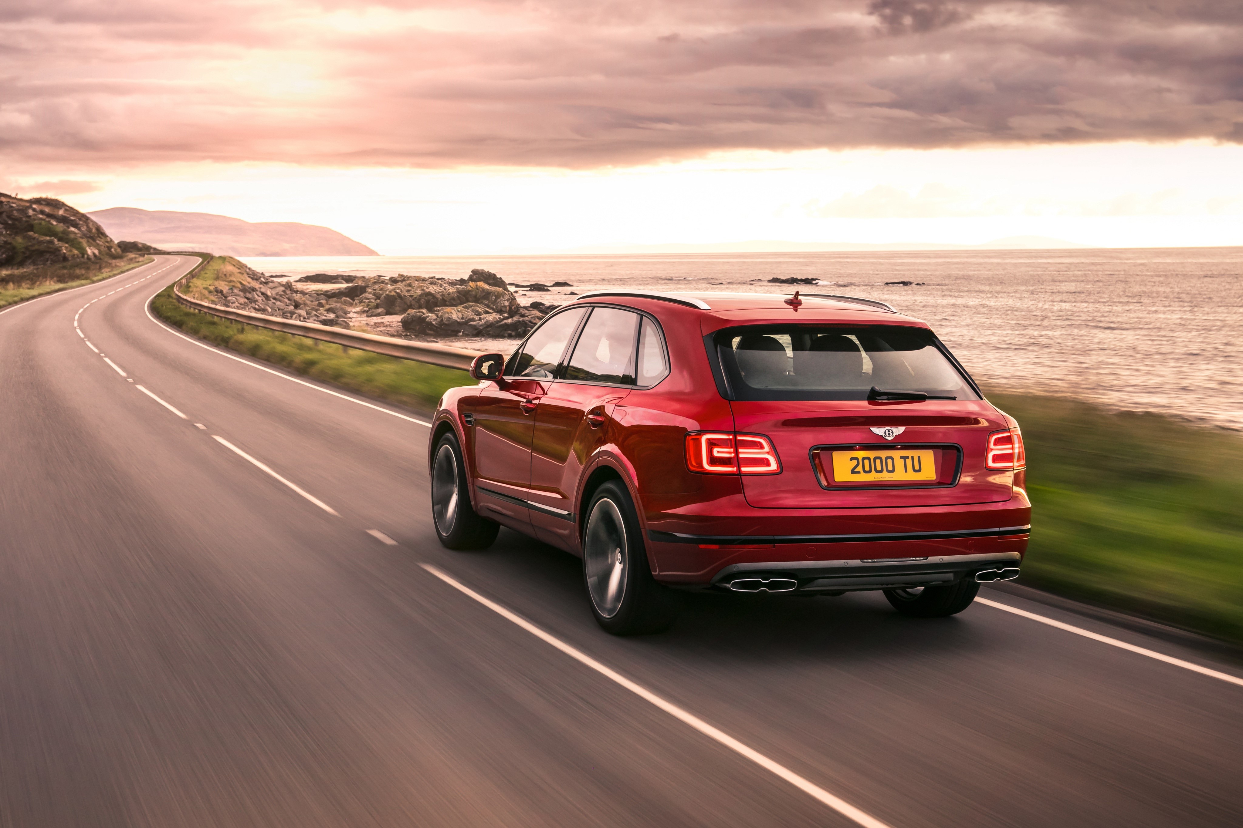 Red Bentley Bentayga driving on coastal road HD Wallpaper