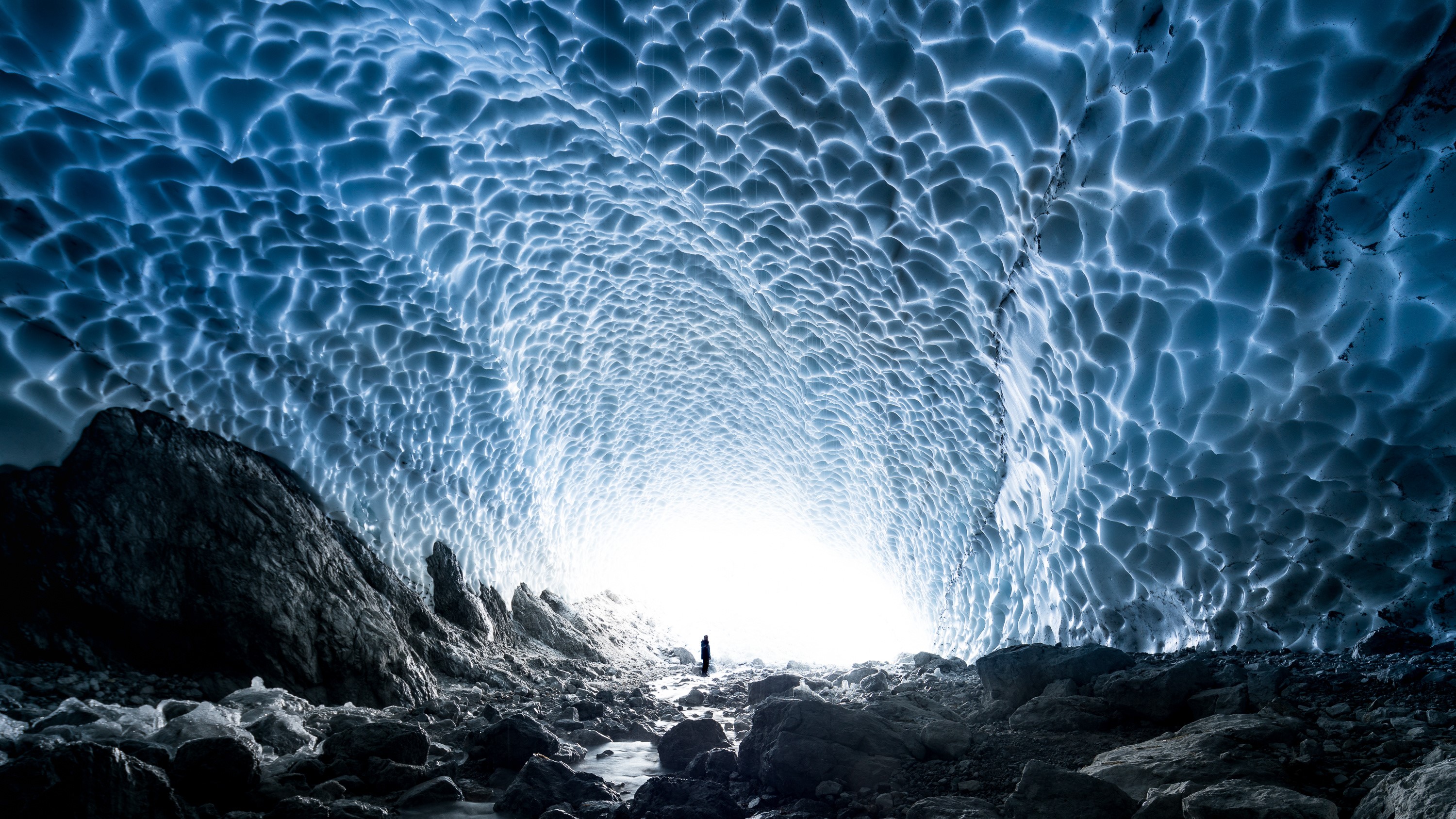 Ice cave with a person standing at the entrance HD Wallpaper