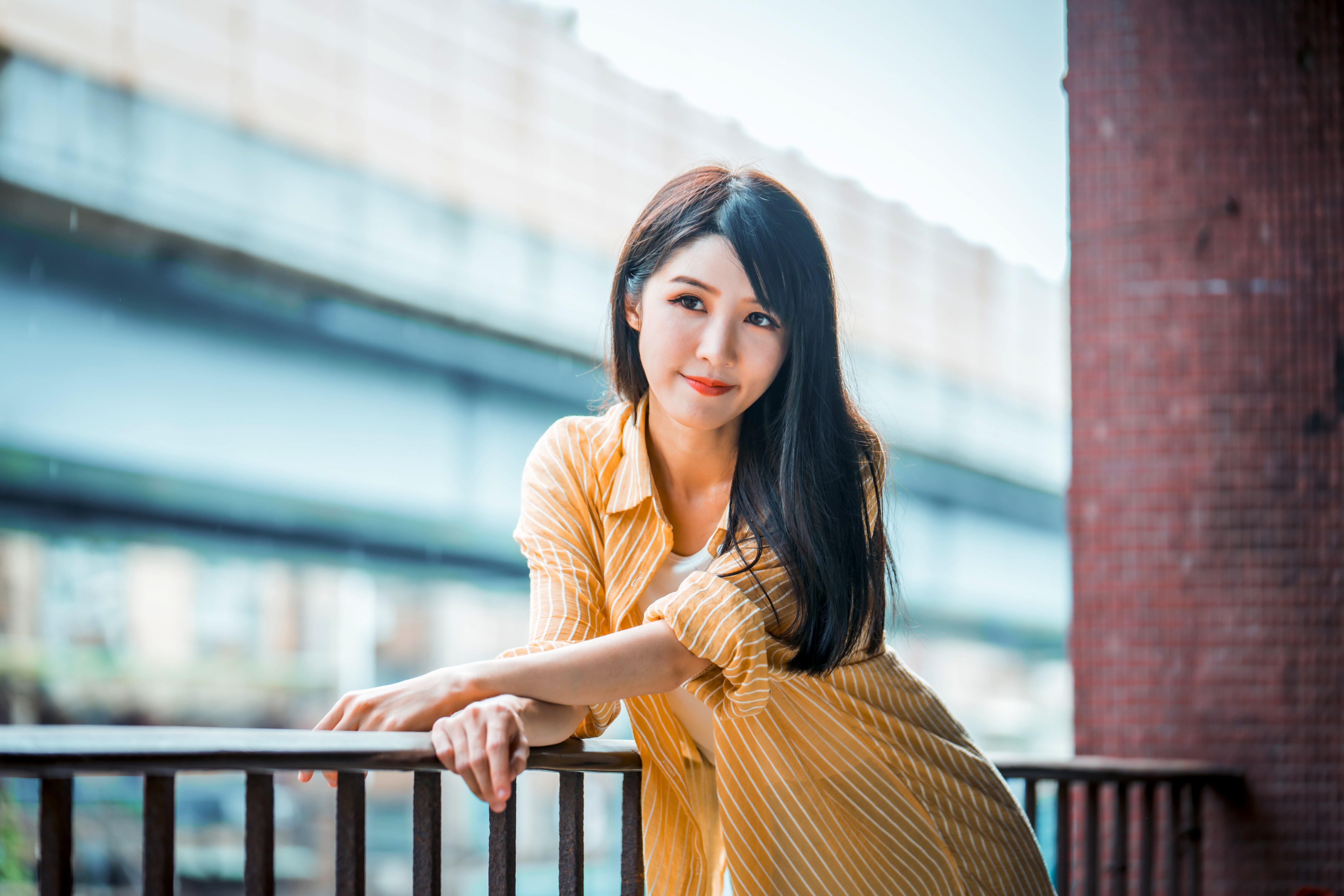 Asian woman in yellow shirt leaning on railing HD Wallpaper