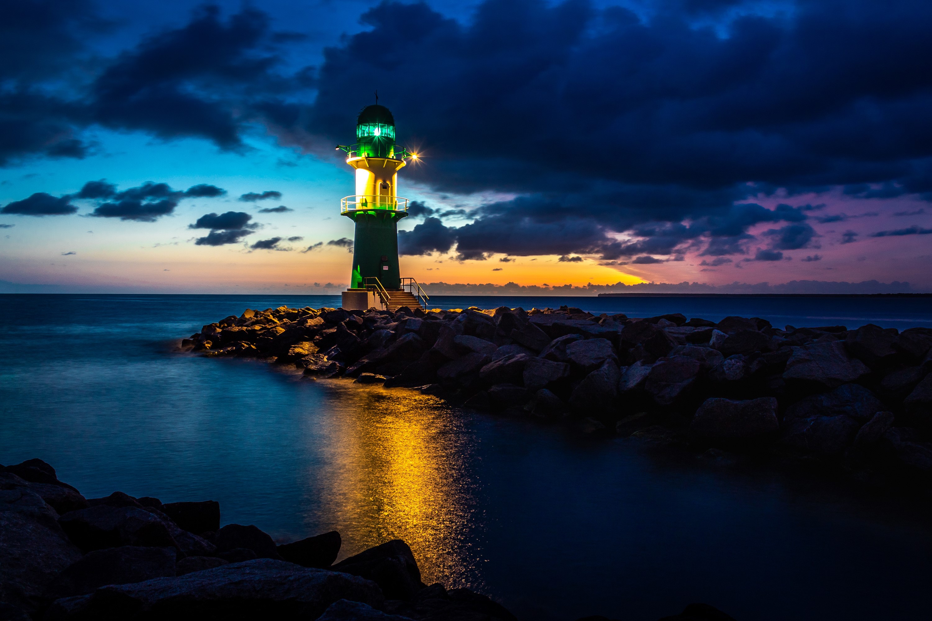 Lighthouse on a rocky shore at dusk in Rostock, Germany HD Wallpaper
