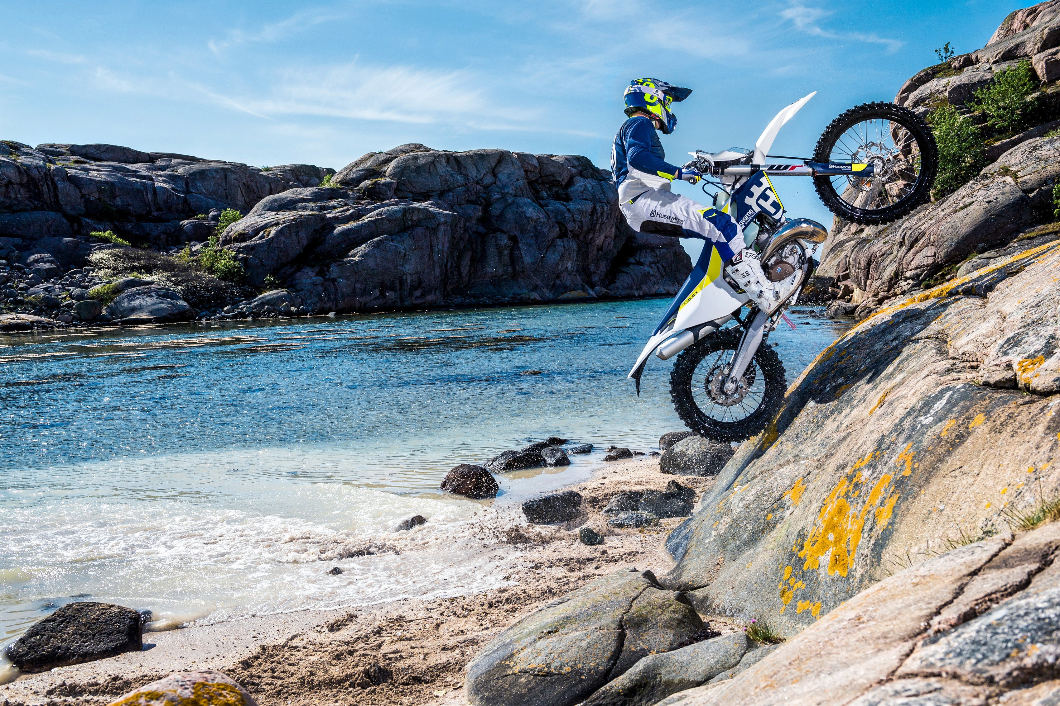 Husqvarna TE 300 motorcyclist performing a wheelie on rocky coast HD Wallpaper