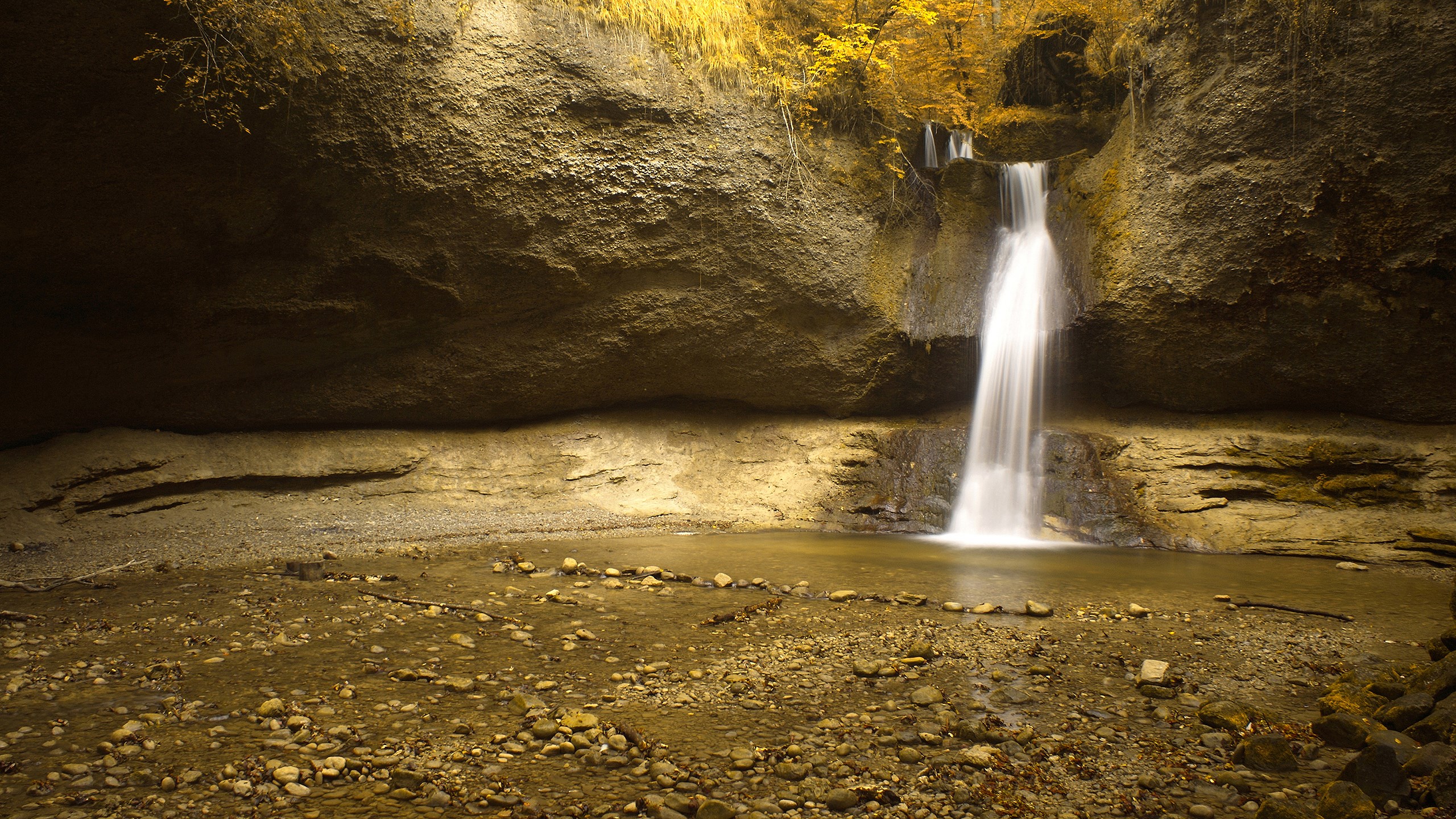 Waterfall cascading into a pool in a rocky grotto HD Wallpaper