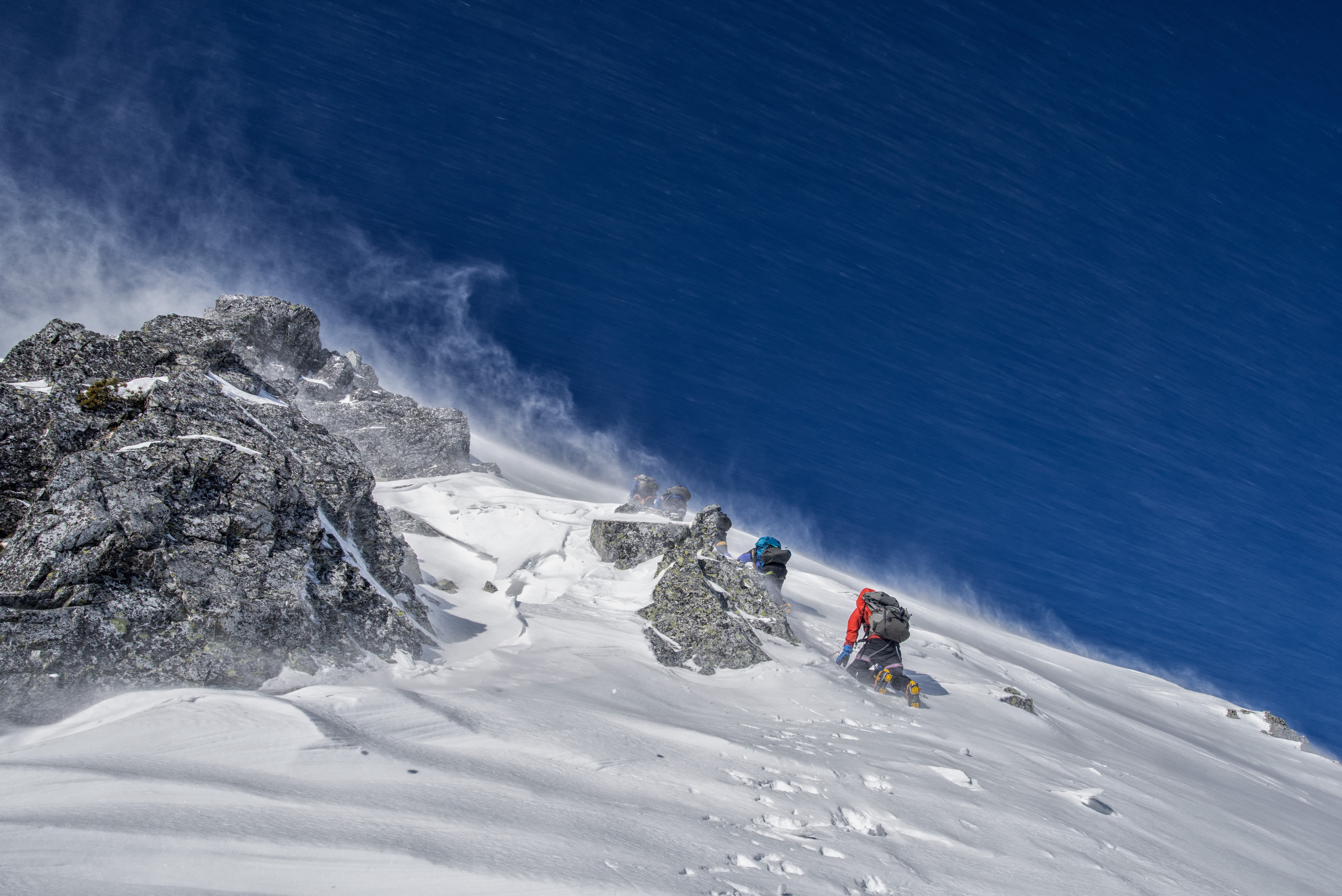 Mountaineers climbing a snowy mountain face HD Wallpaper