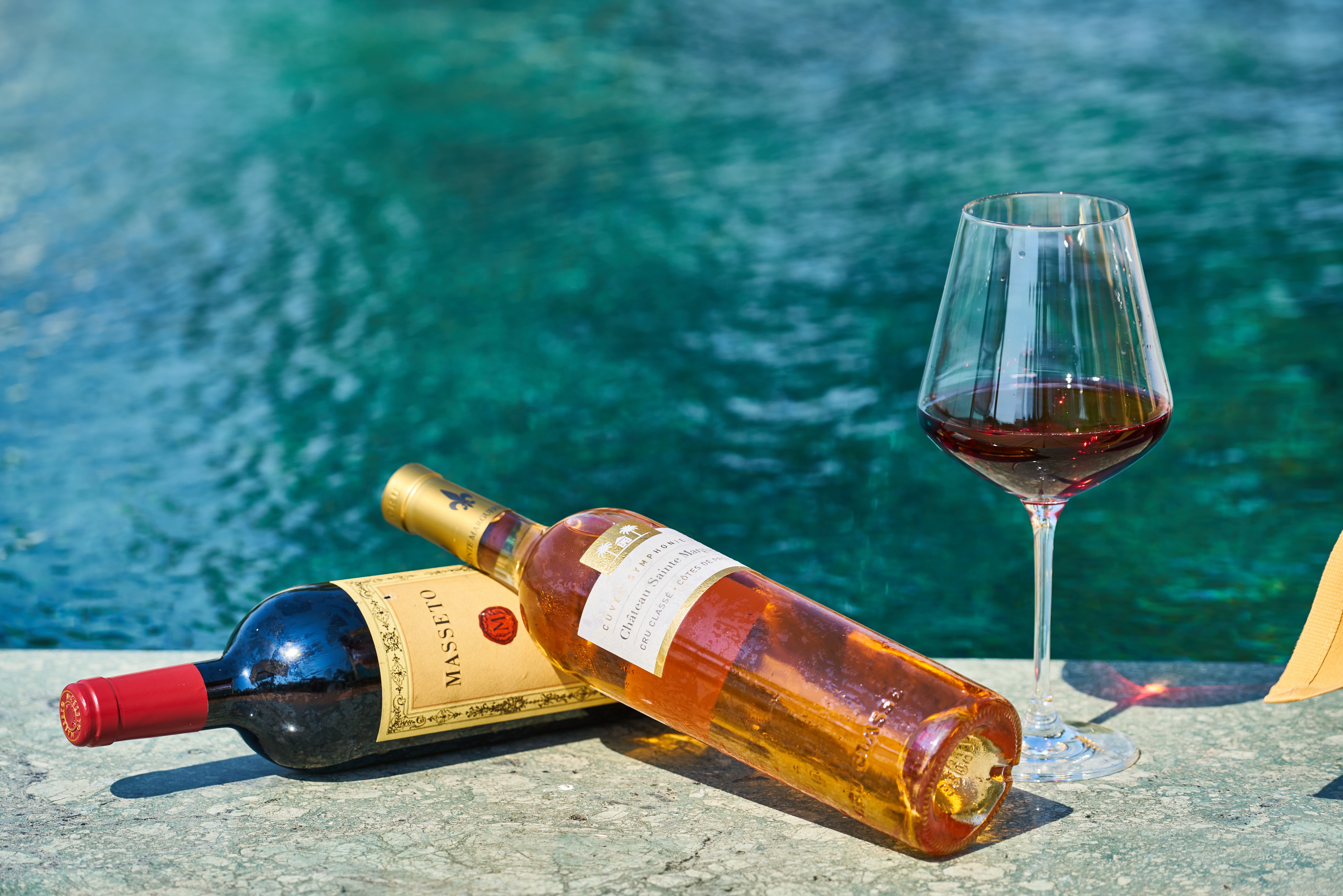 Two wine bottles and a glass of red wine by the pool HD Wallpaper