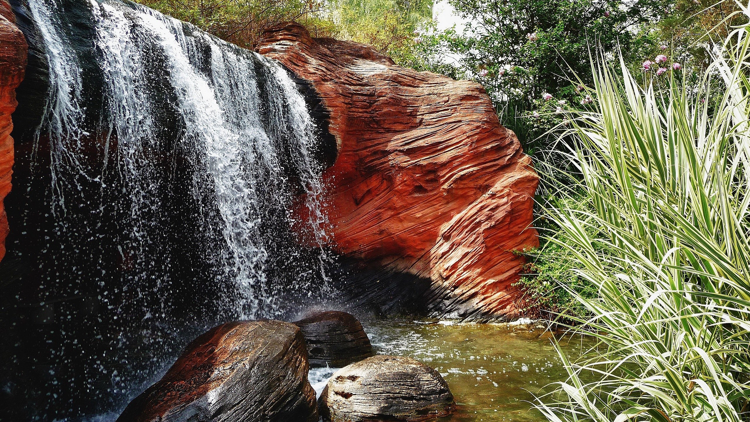 Waterfall cascading over red rocks with plants HD Wallpaper