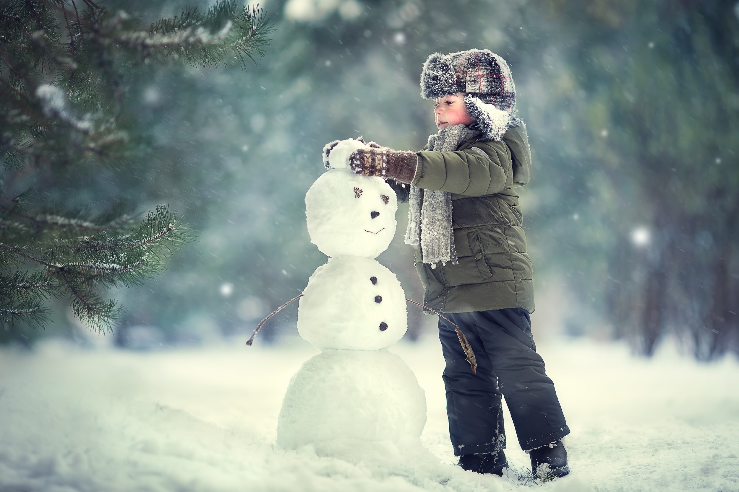 Boy building a snowman in a snowy forest HD Wallpaper