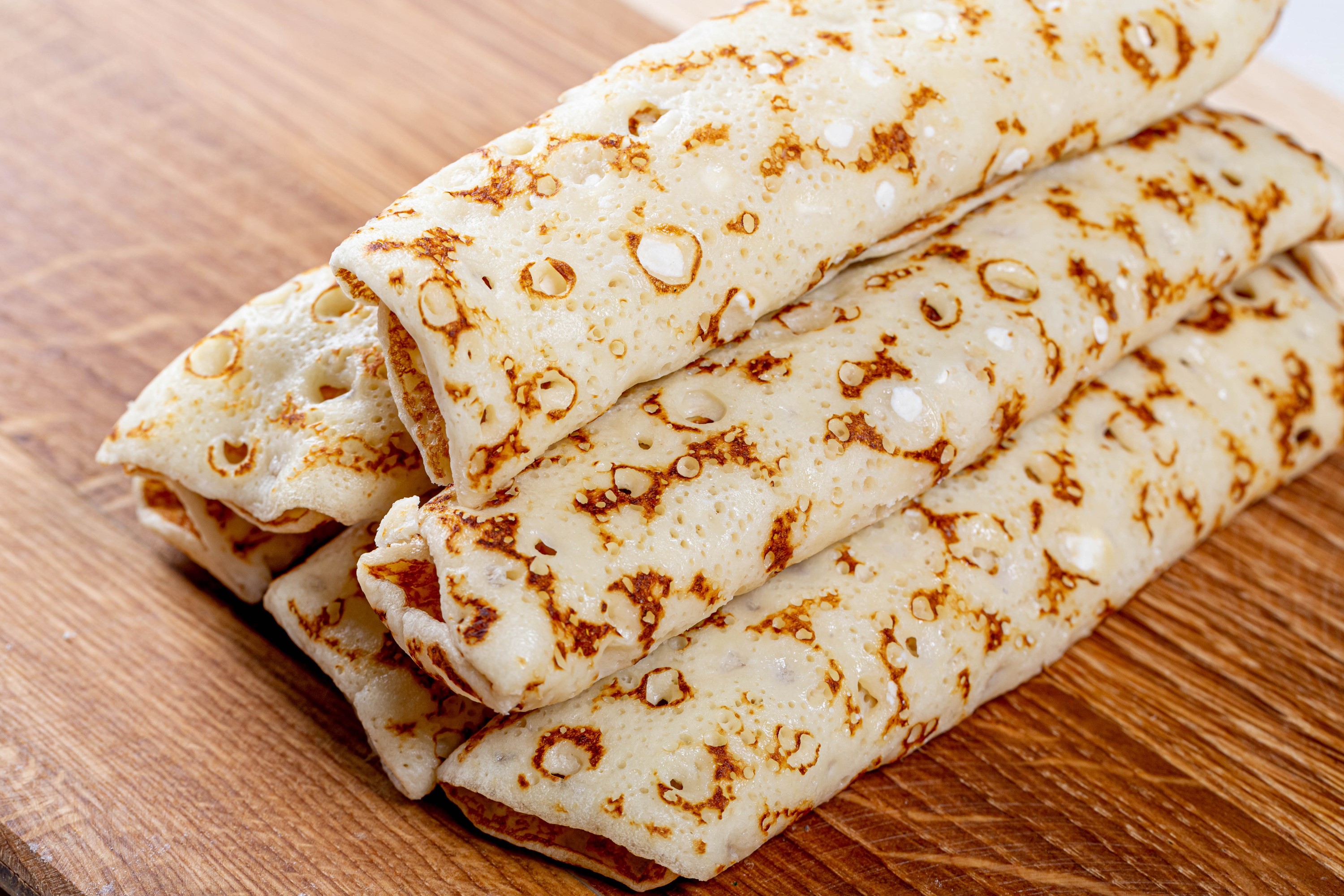Rolled pancakes stacked on a wooden cutting board HD Wallpaper