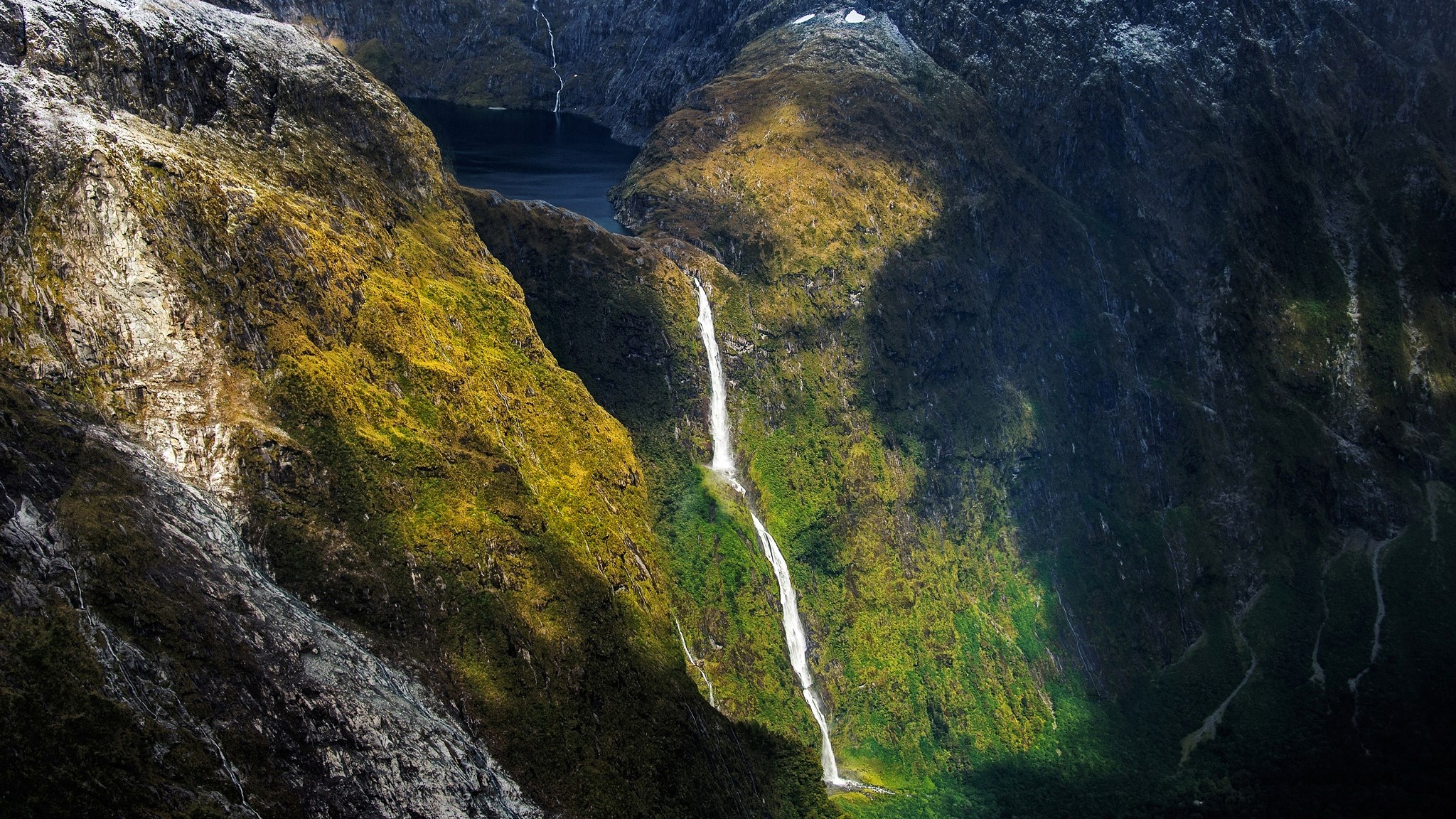 Waterfalls cascading down a moss-covered mountain into a dark lake HD Wallpaper