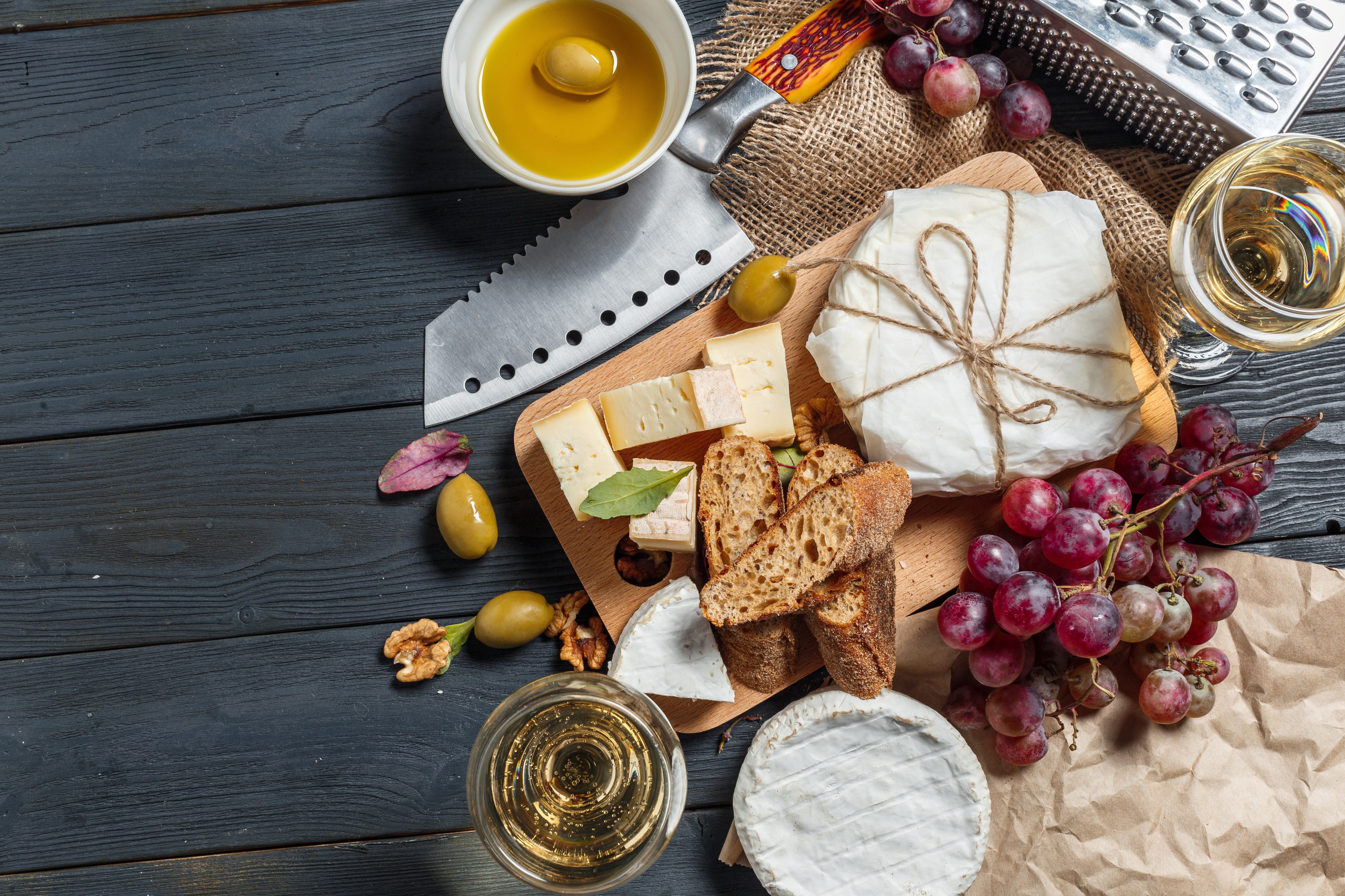 Cheese, Bread, Grapes, Wine, and Olives on a Cutting Board HD Wallpaper