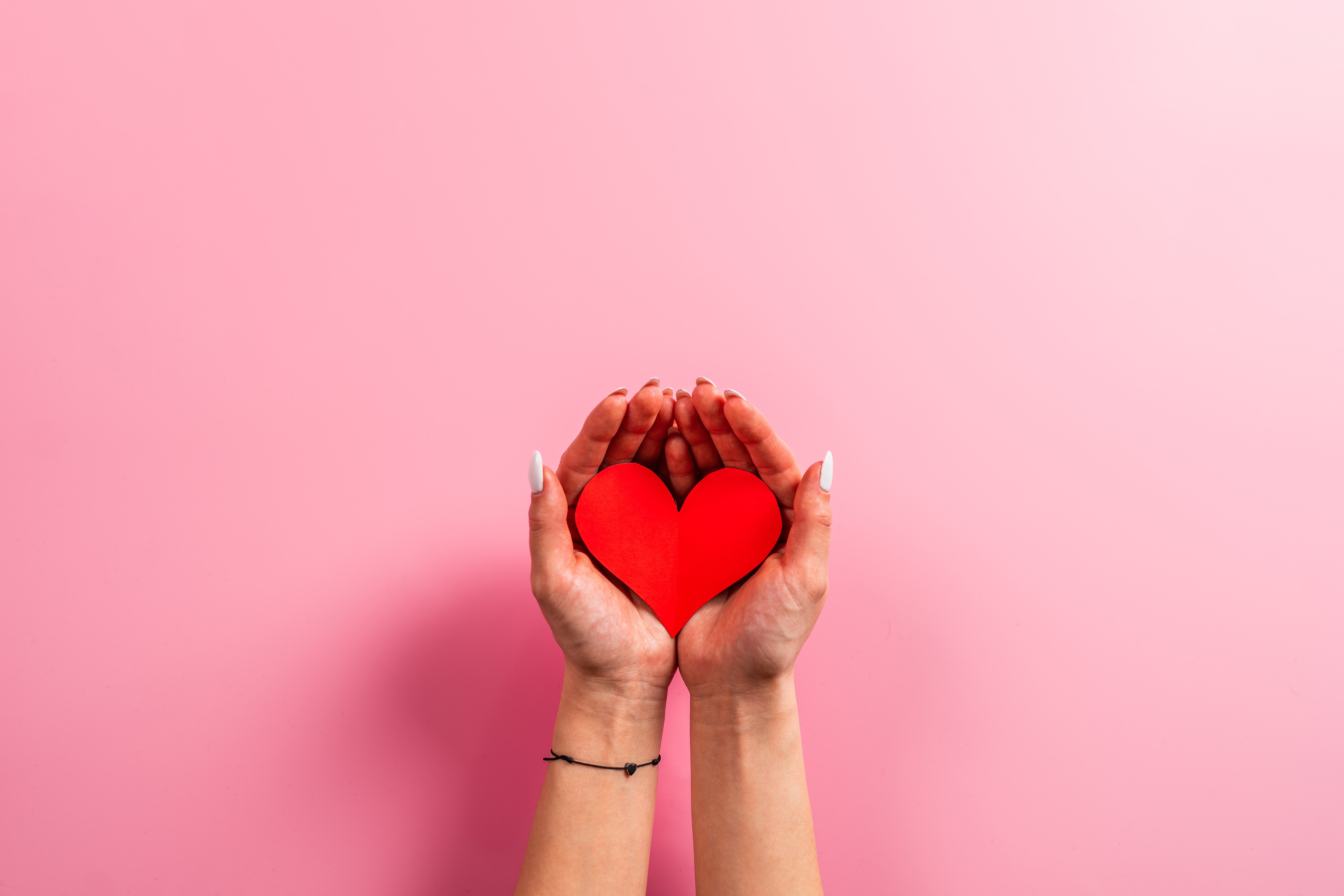 Hands holding a red heart on a pink background HD Wallpaper
